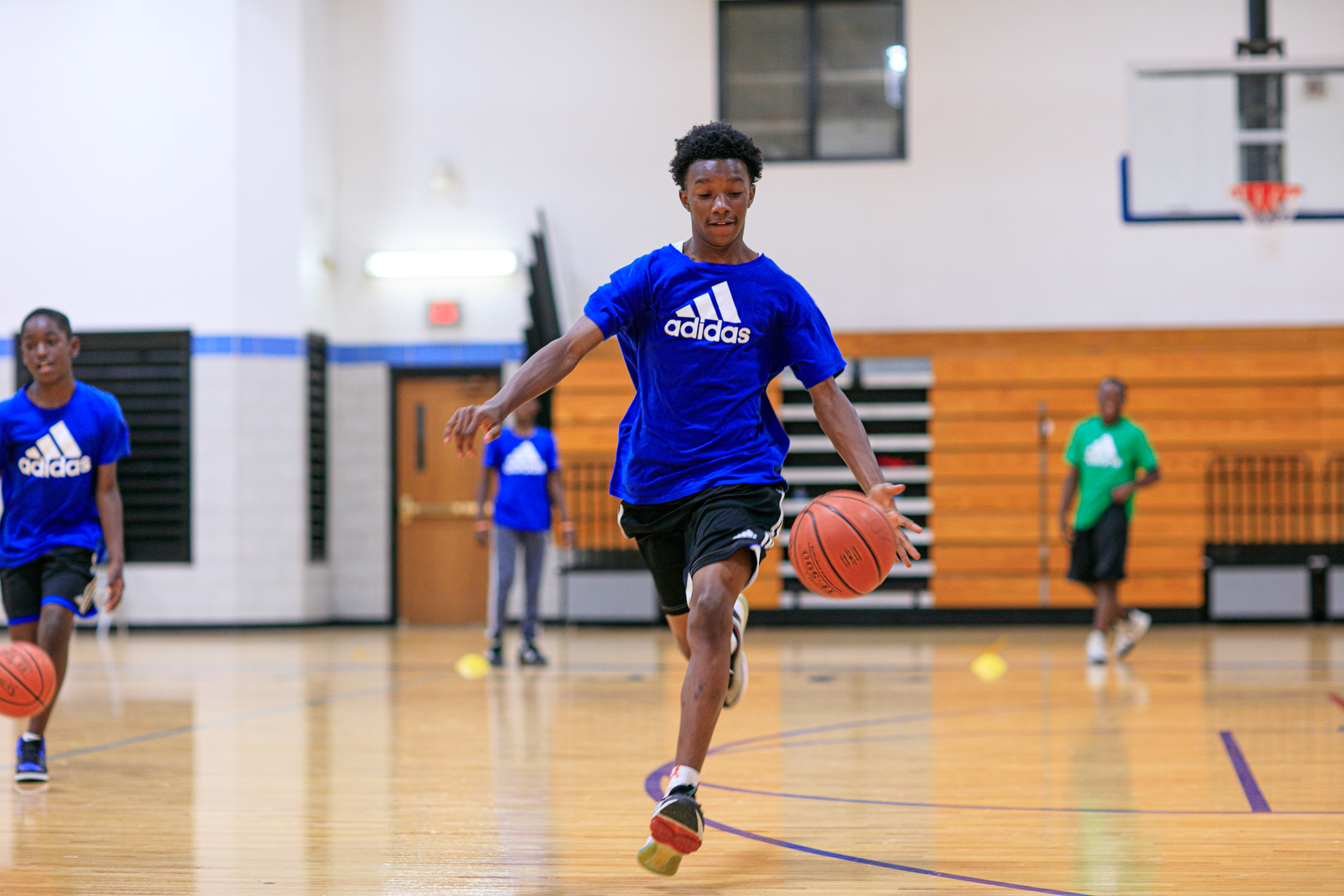 A young man runs across a gym dribbling a basketball