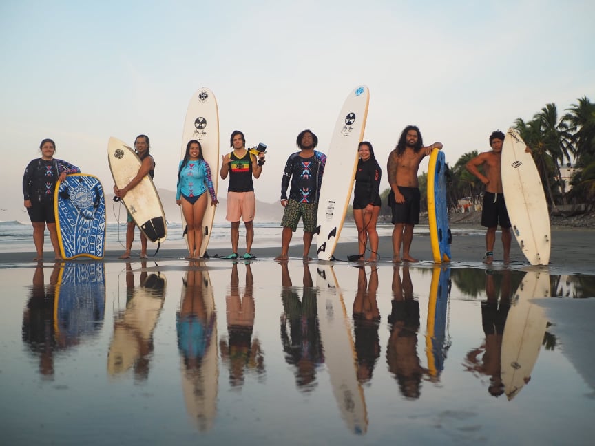 A group of teens stand holding upright surf boards on a beach