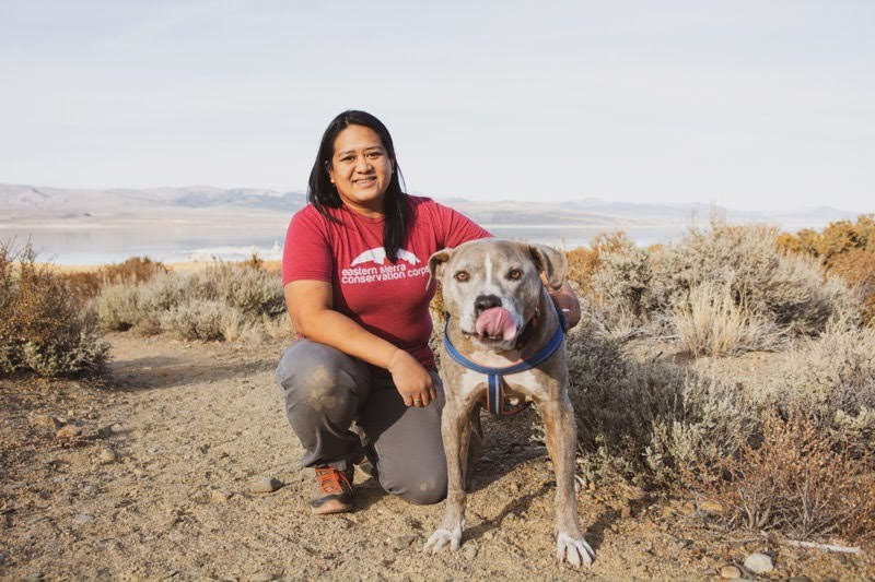 A person in an ESCC shirt kneels outside with a dog