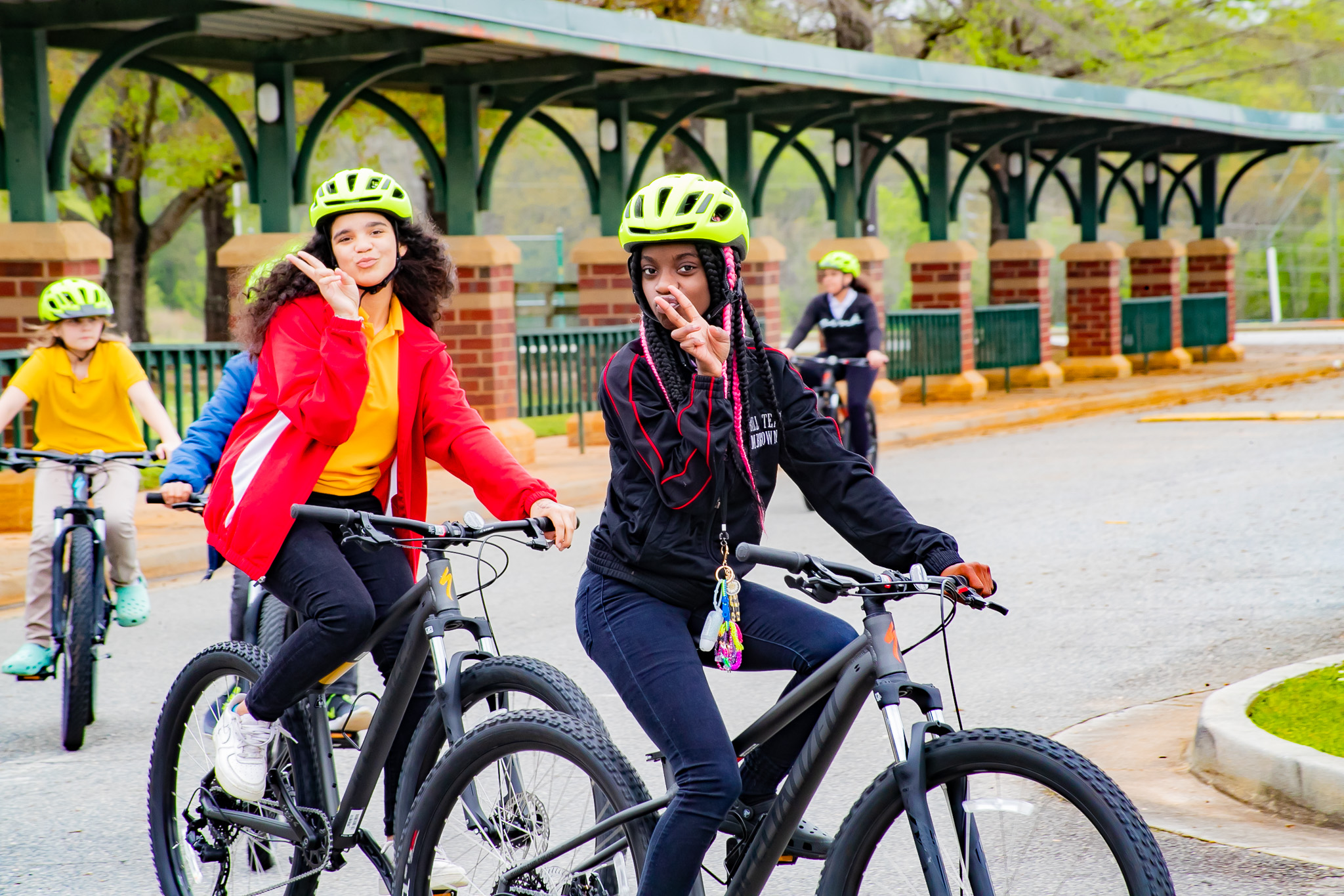 two young people bike past the camera while holding up peace signs