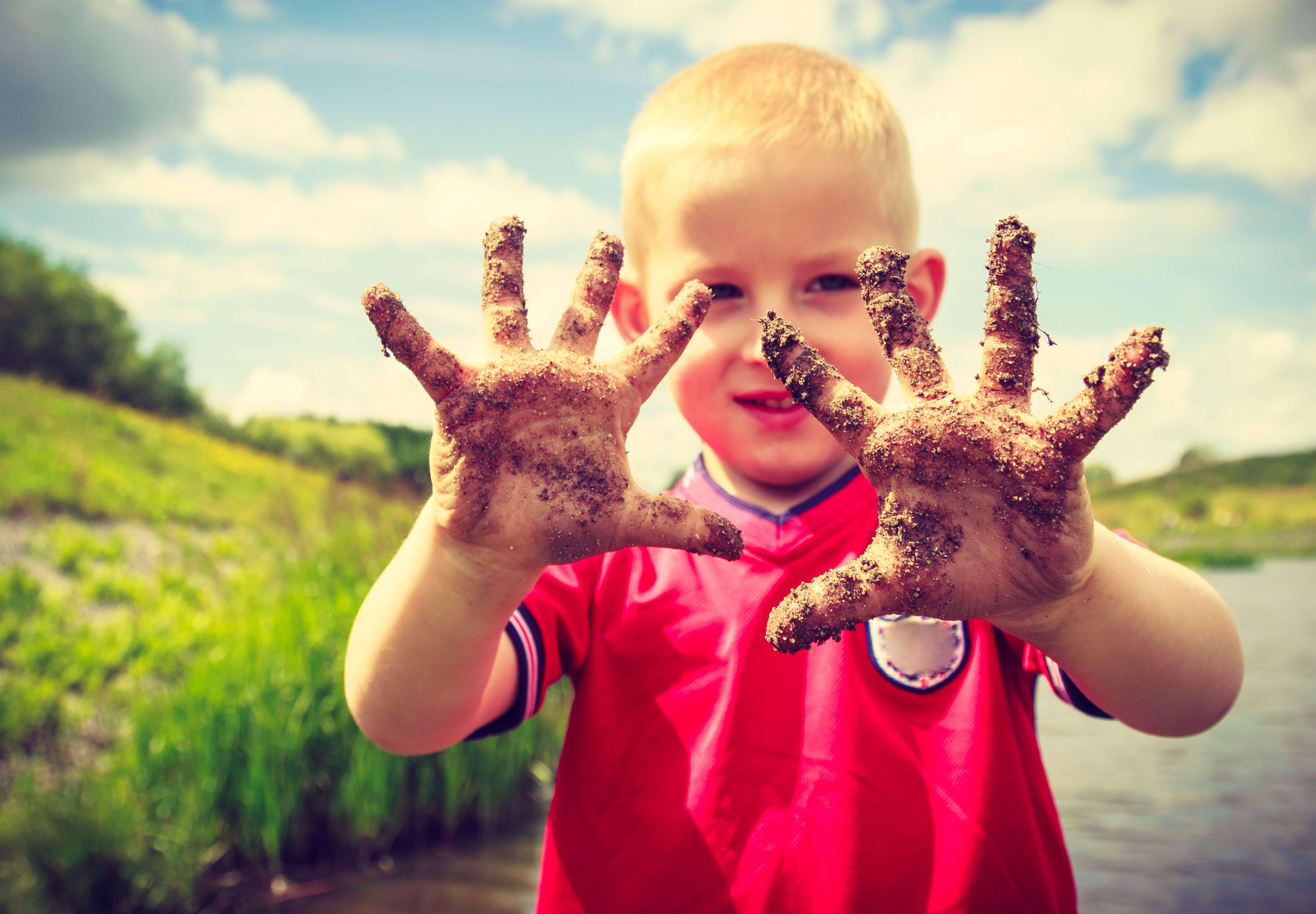 A child holds muddy fingers up to the camera