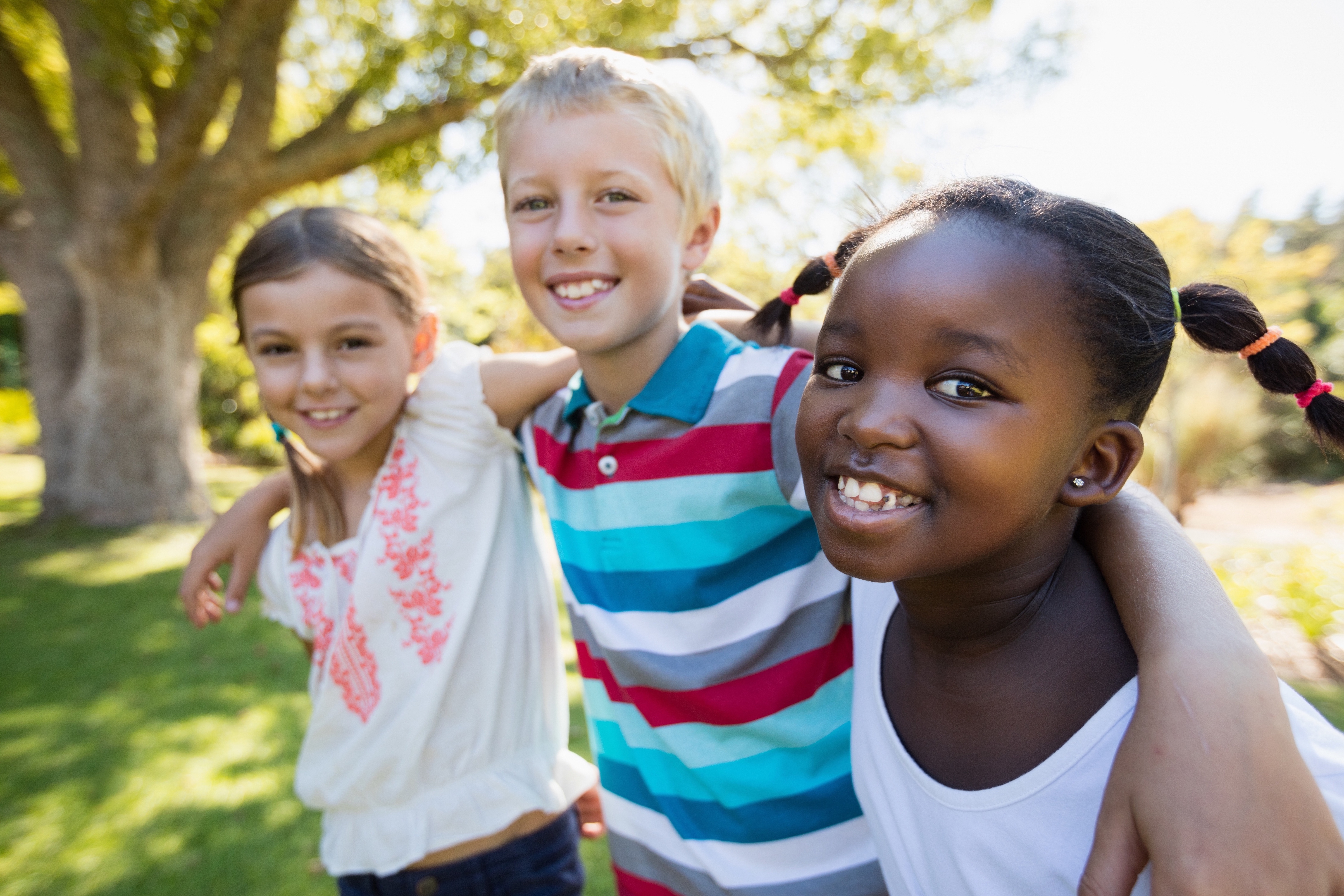 three kids smile with their arms around each other