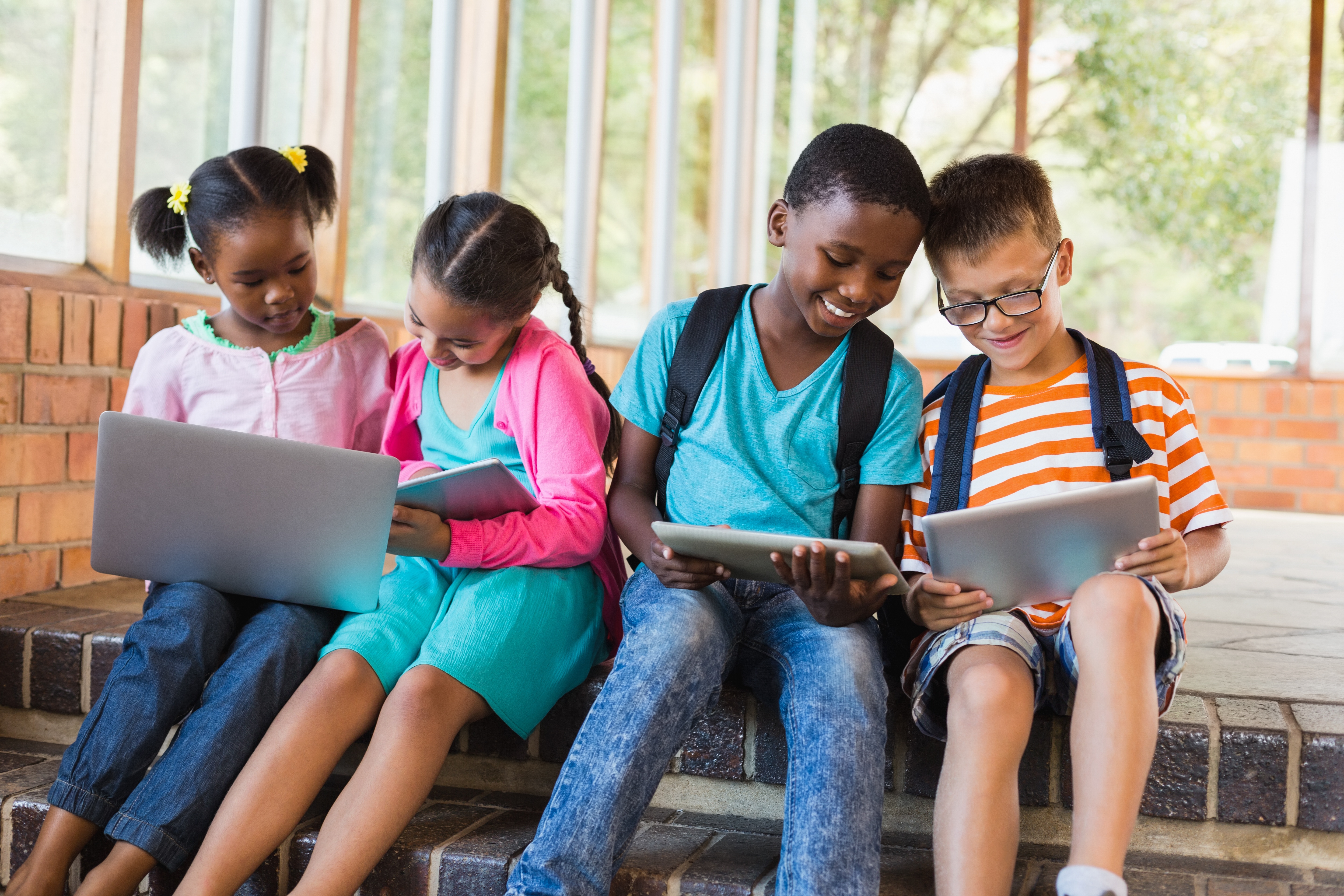 Kids sit with technology on steps outside