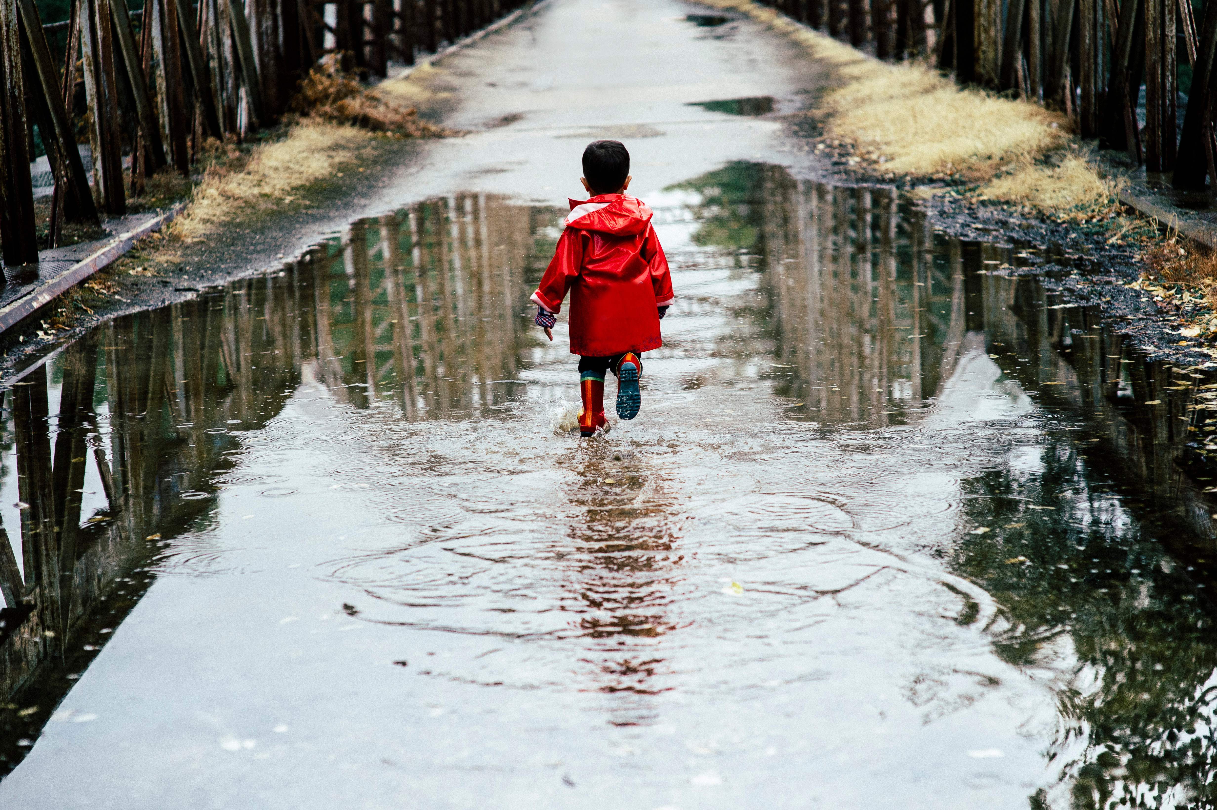 A young child runs through a puddle while wearing rain gear