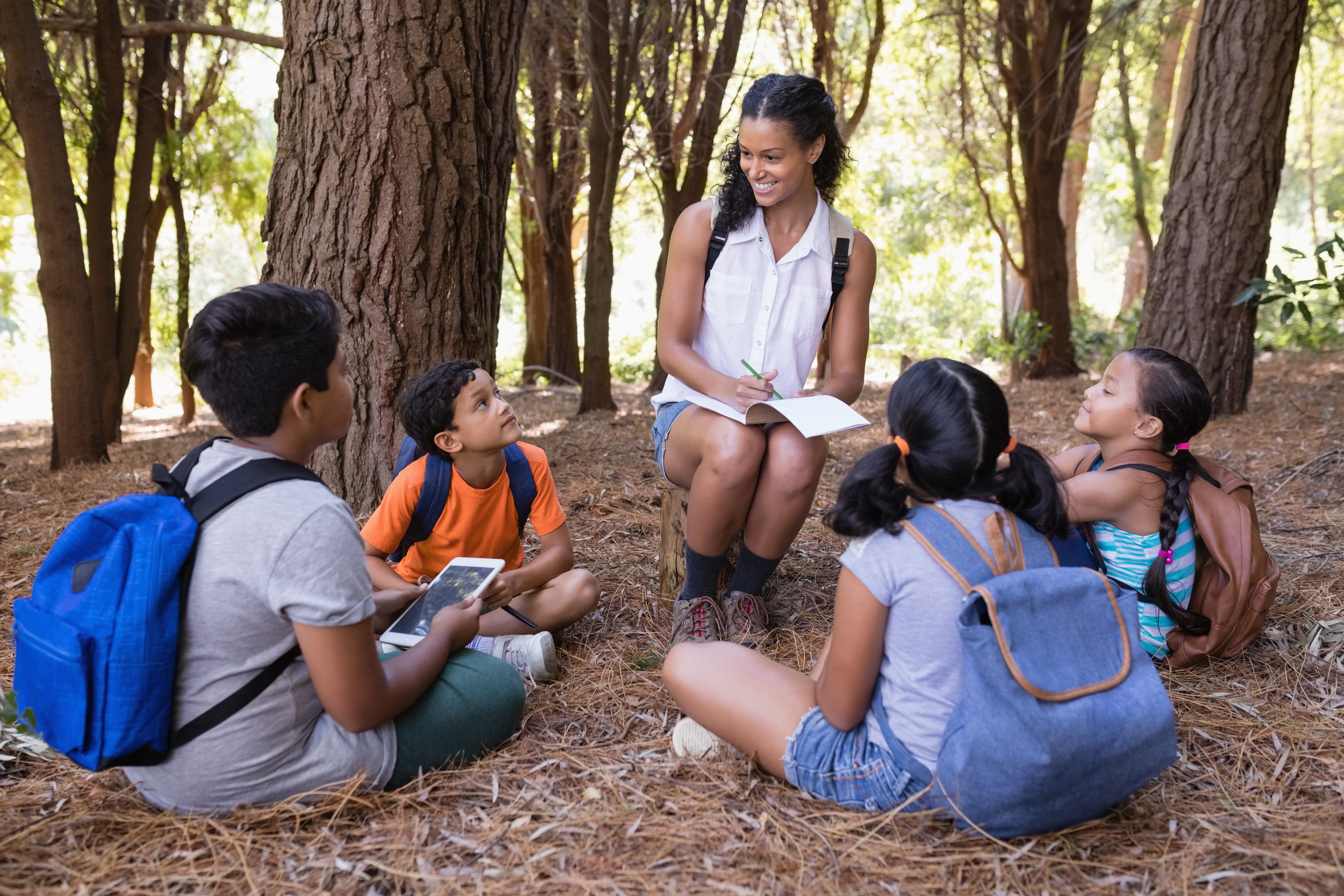 An adult sits with a circle of children outside