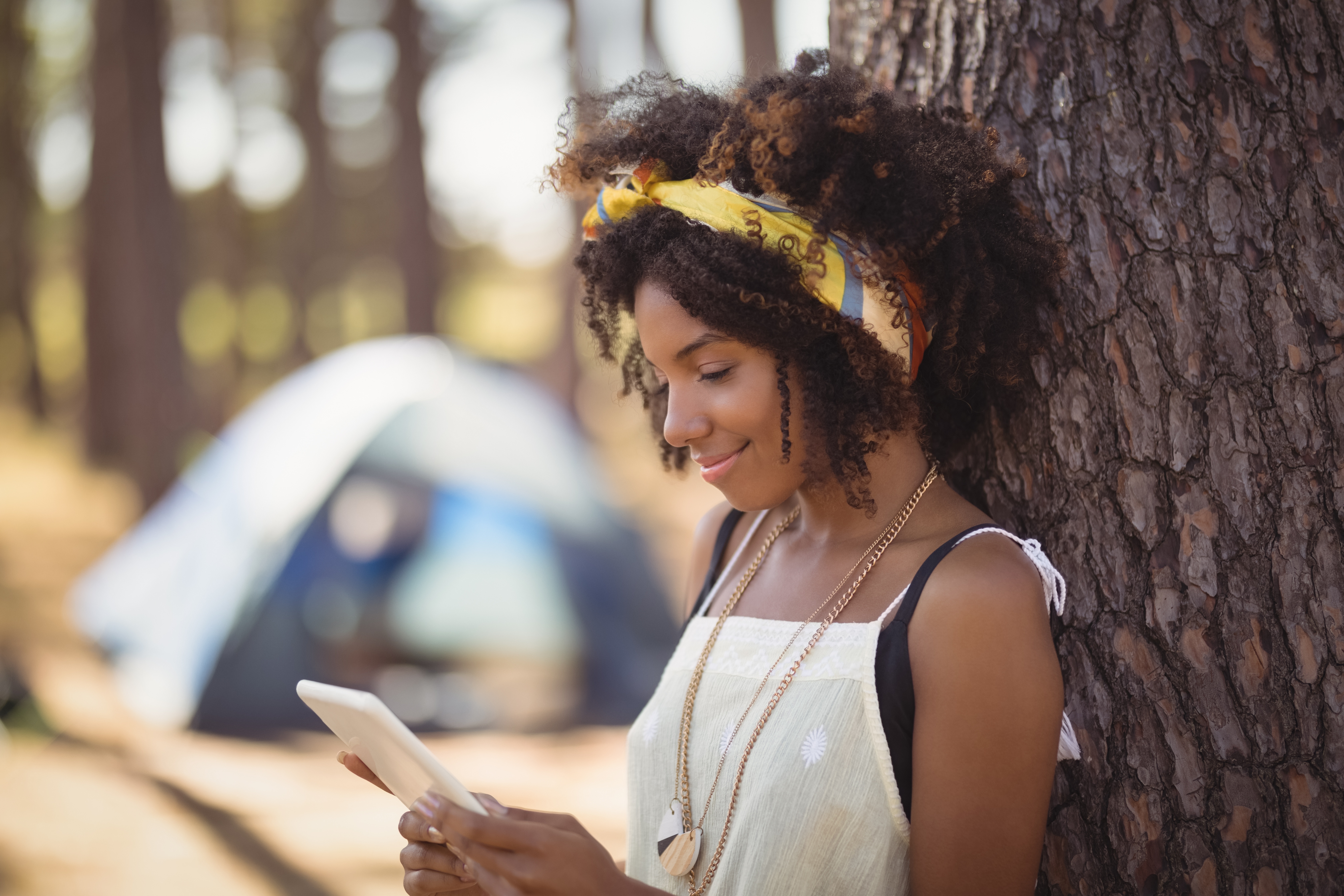 woman with tablet leaning against a tree