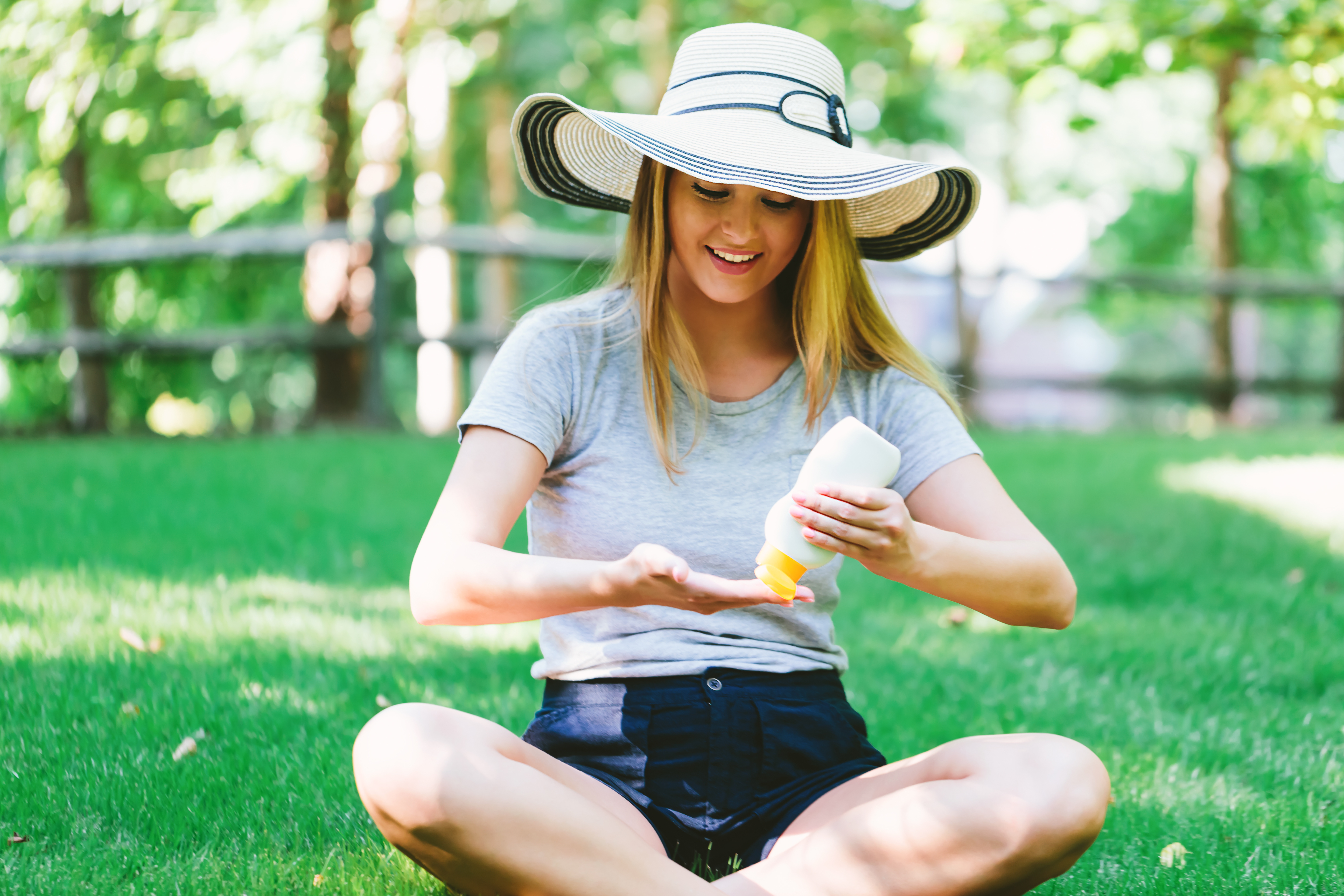 a young woman applies sunscreen while wearing a large hat