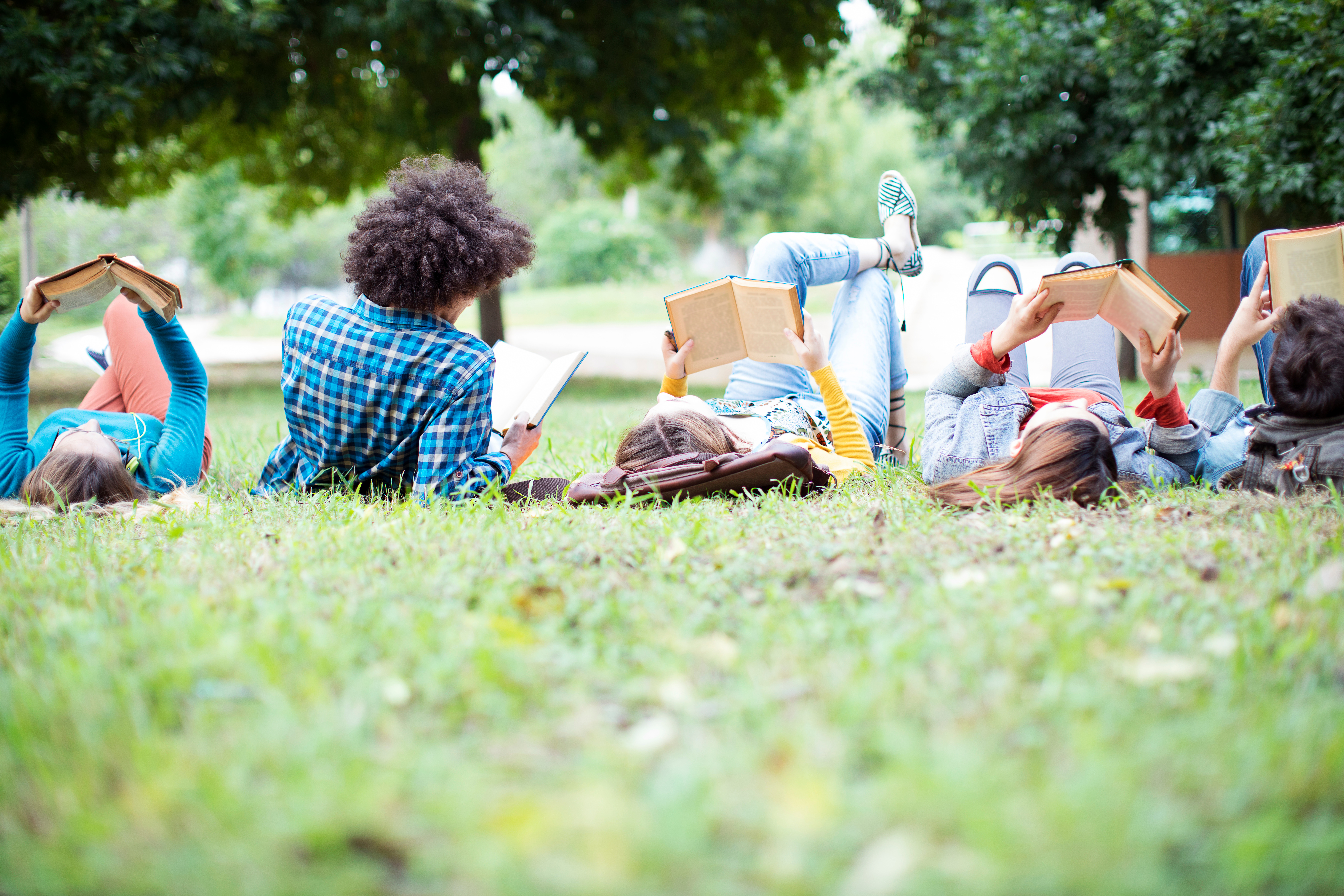 Teenagers lay in the grass in a park reading books