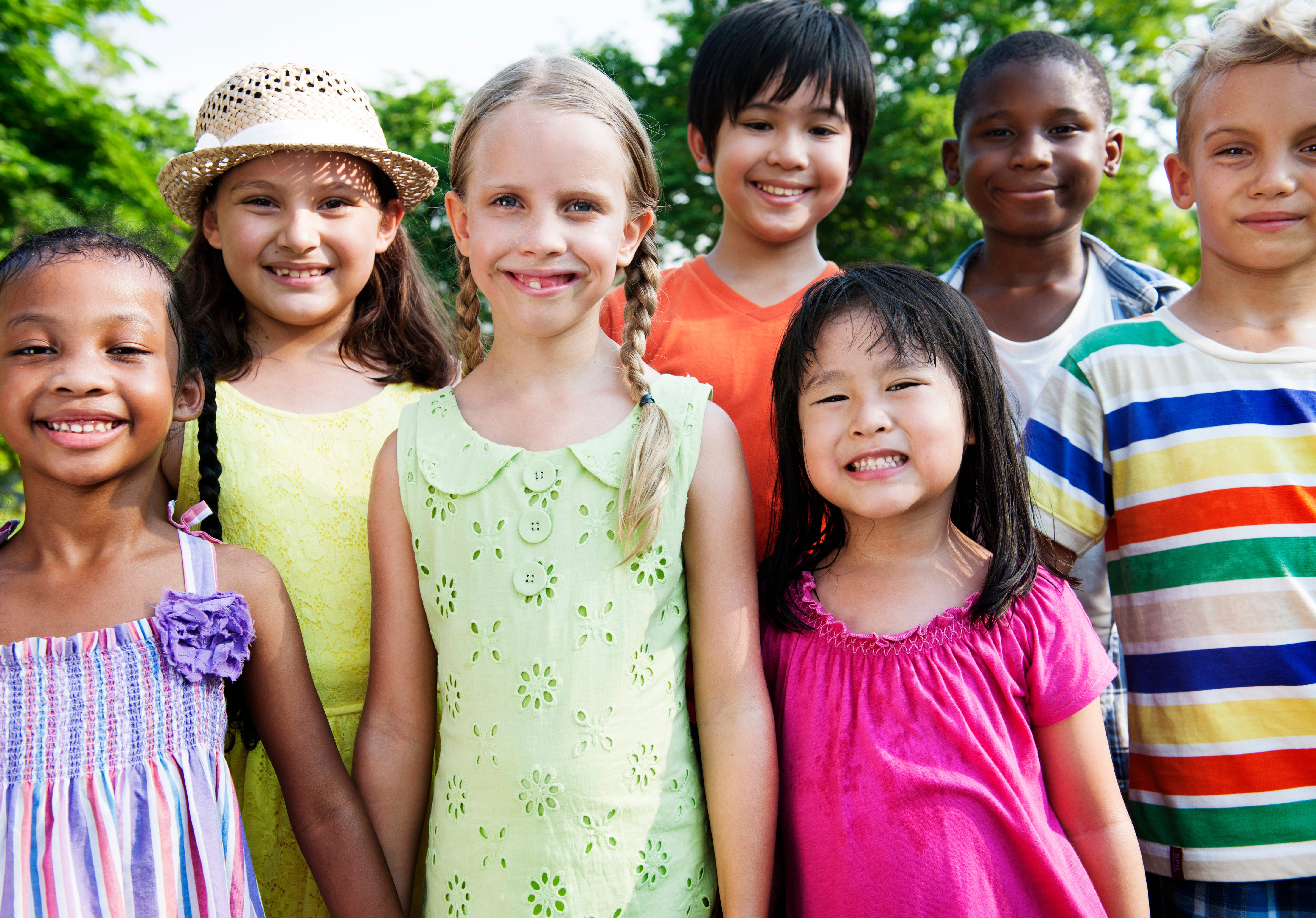 A group of children stands outside and smiles at the camera