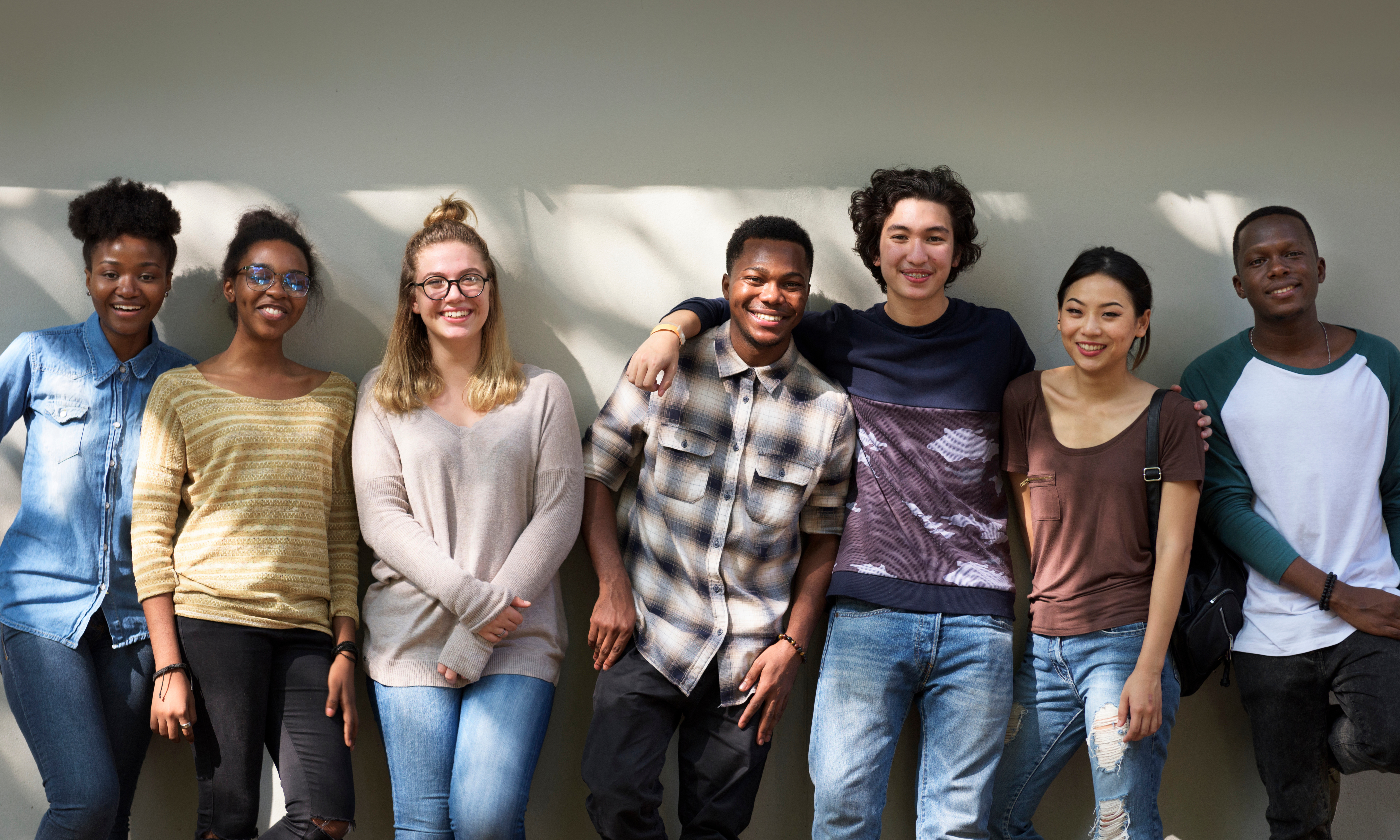 A line of youth stand against a wall and smile