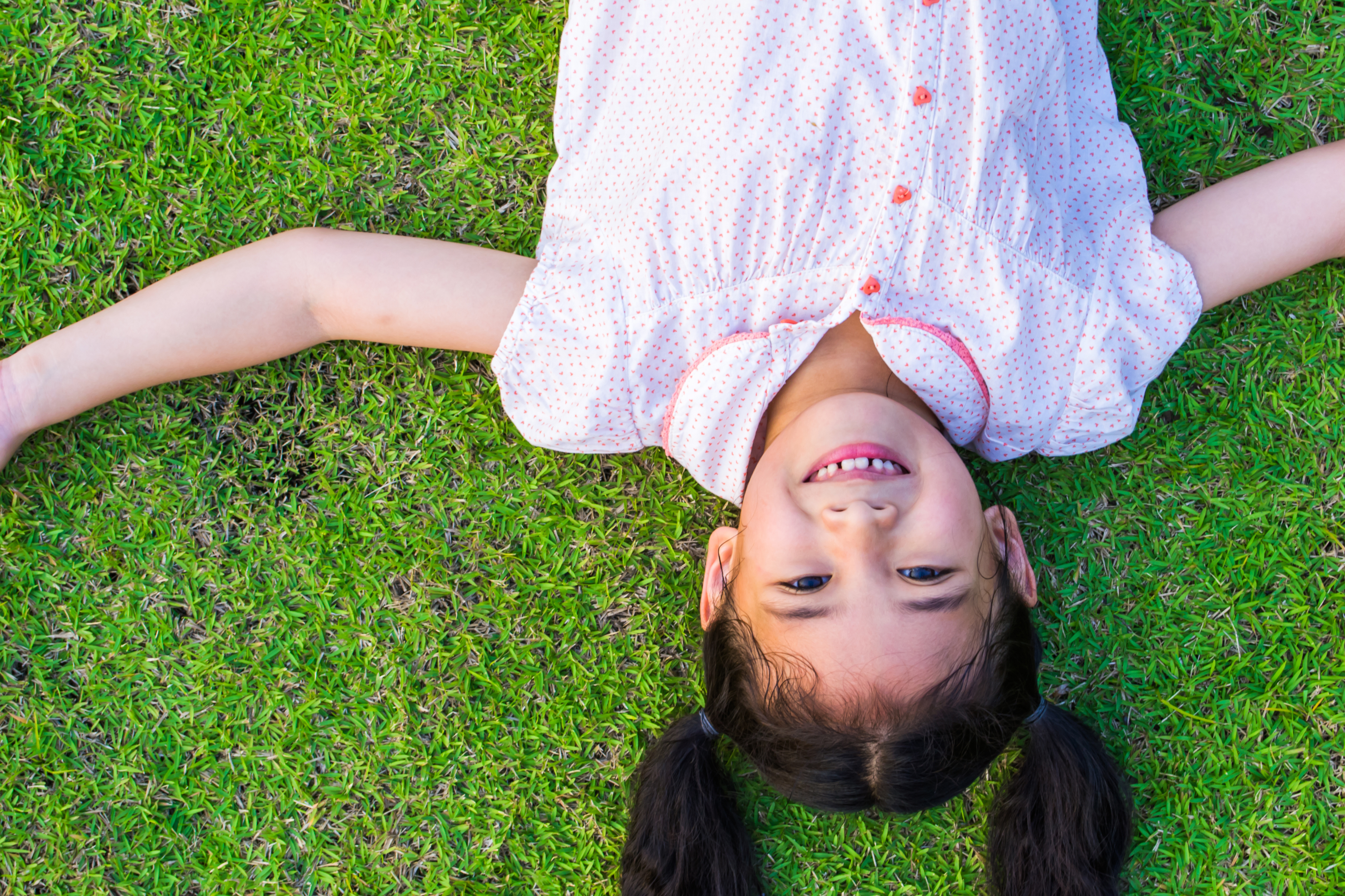 A child smiles up at the camera while laying in grass