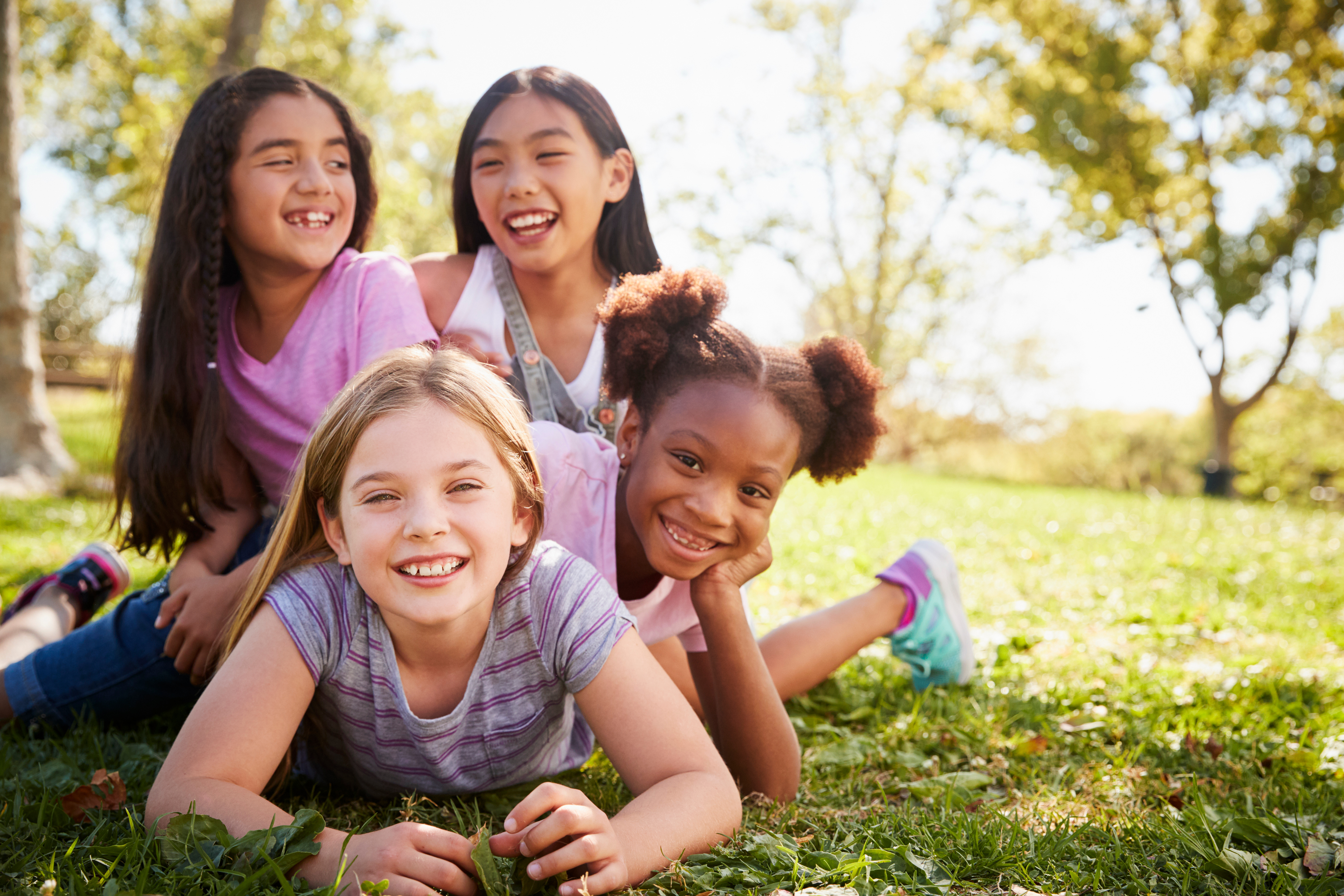 A group of kids lay together outside while smiling
