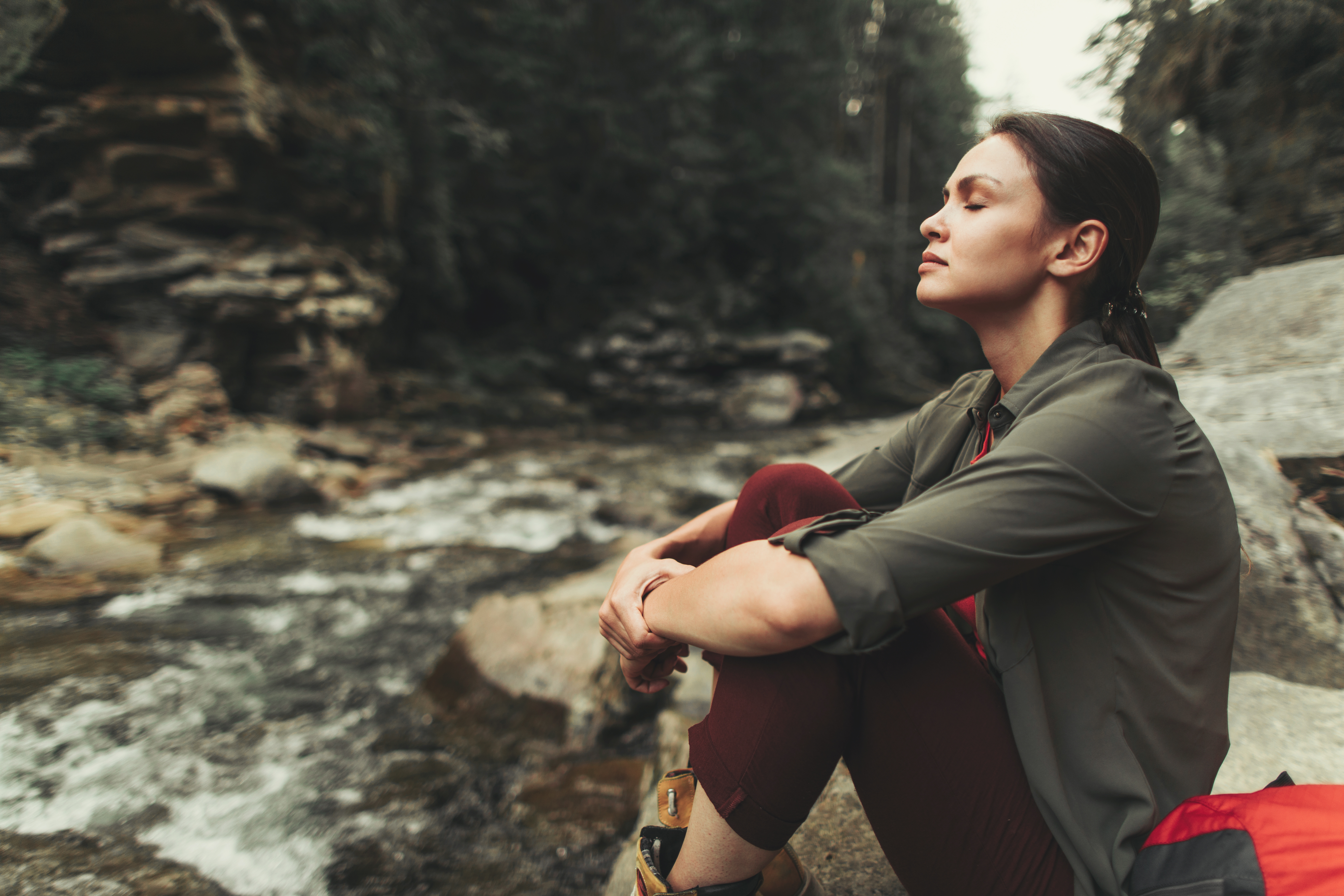 A person sits near a stream, looking serene