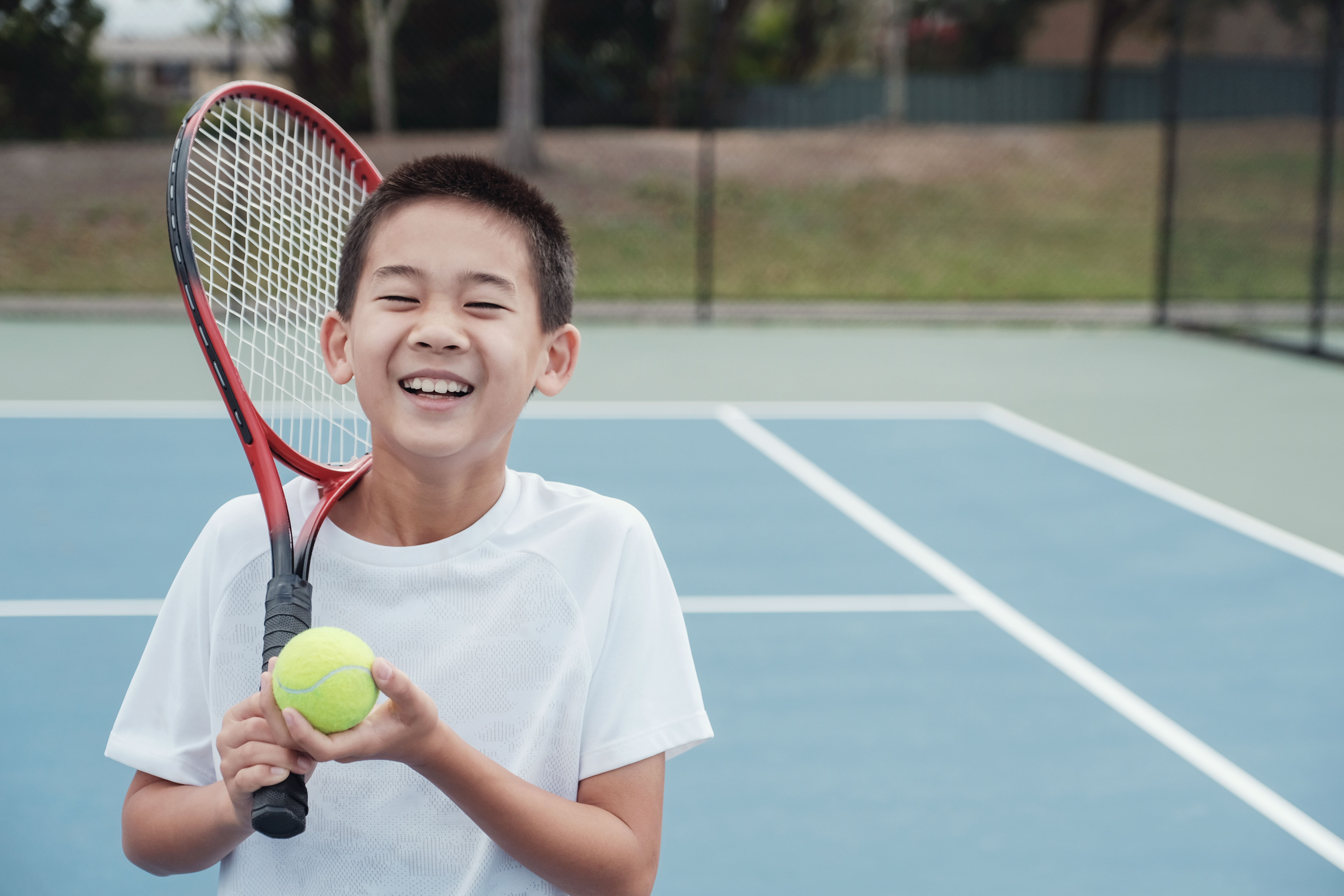 A child stands holding a tennis racket and ball
