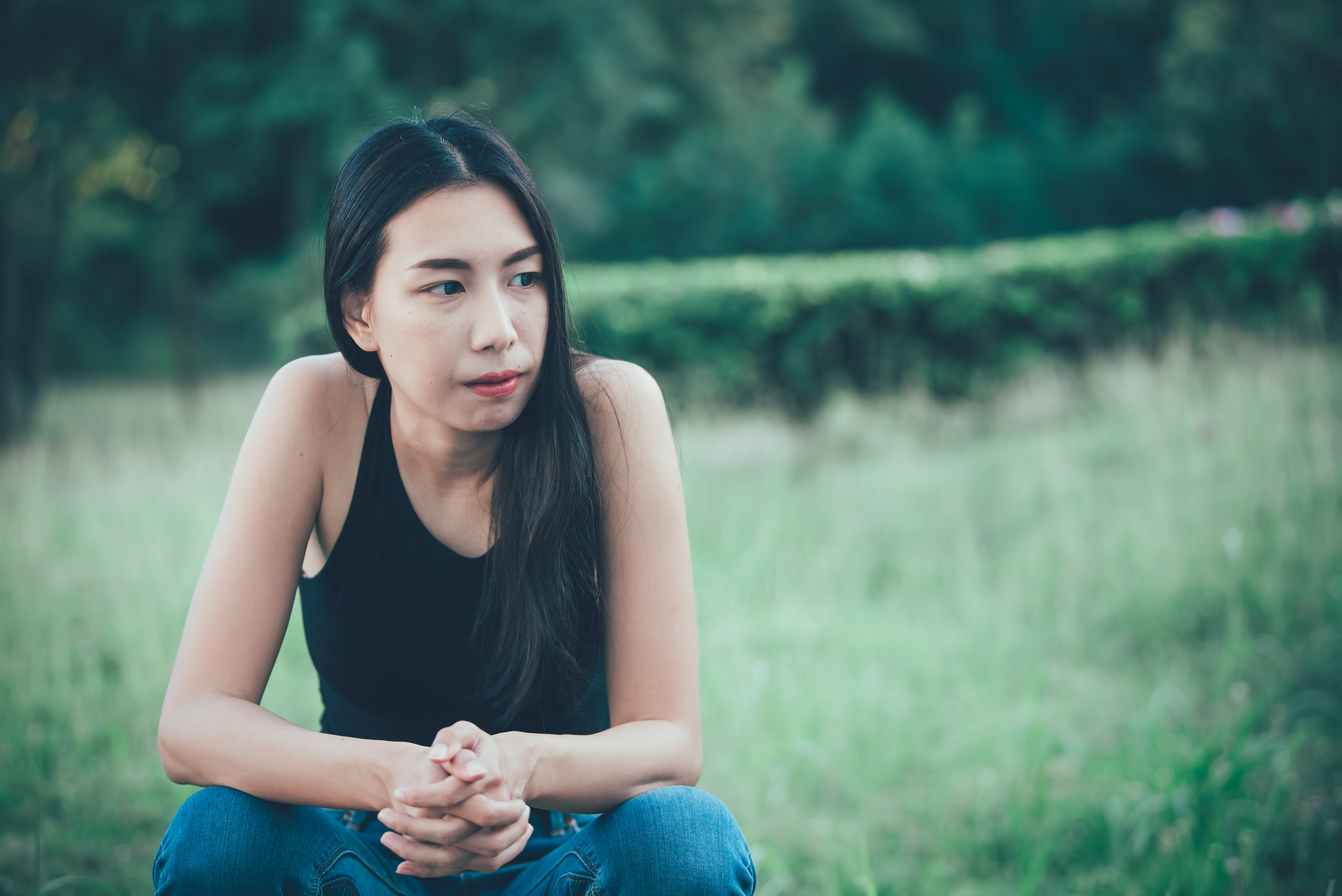 A young person sits looking solemn in long grass