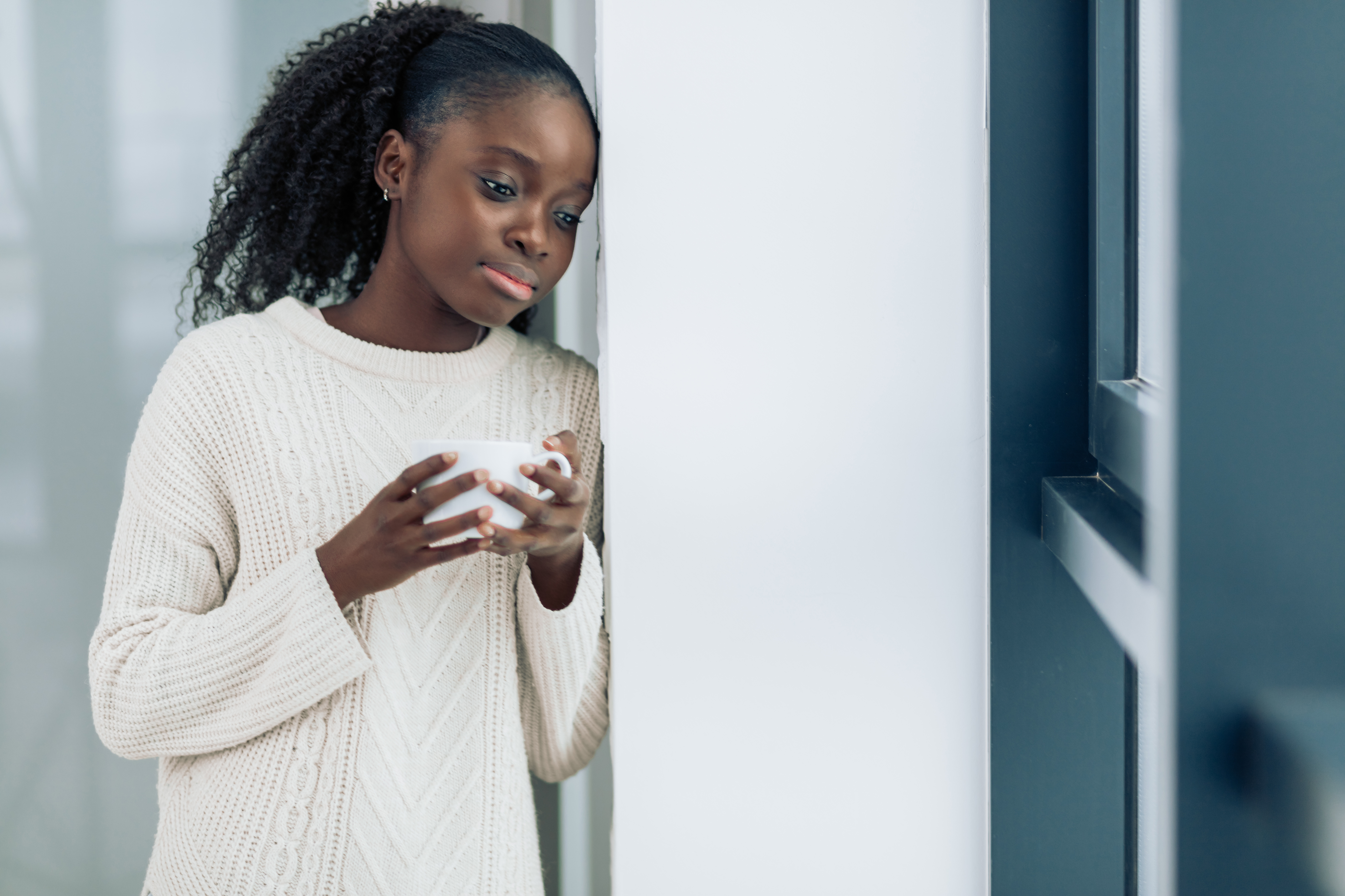 a young woman leans against a wall with a cup of tea