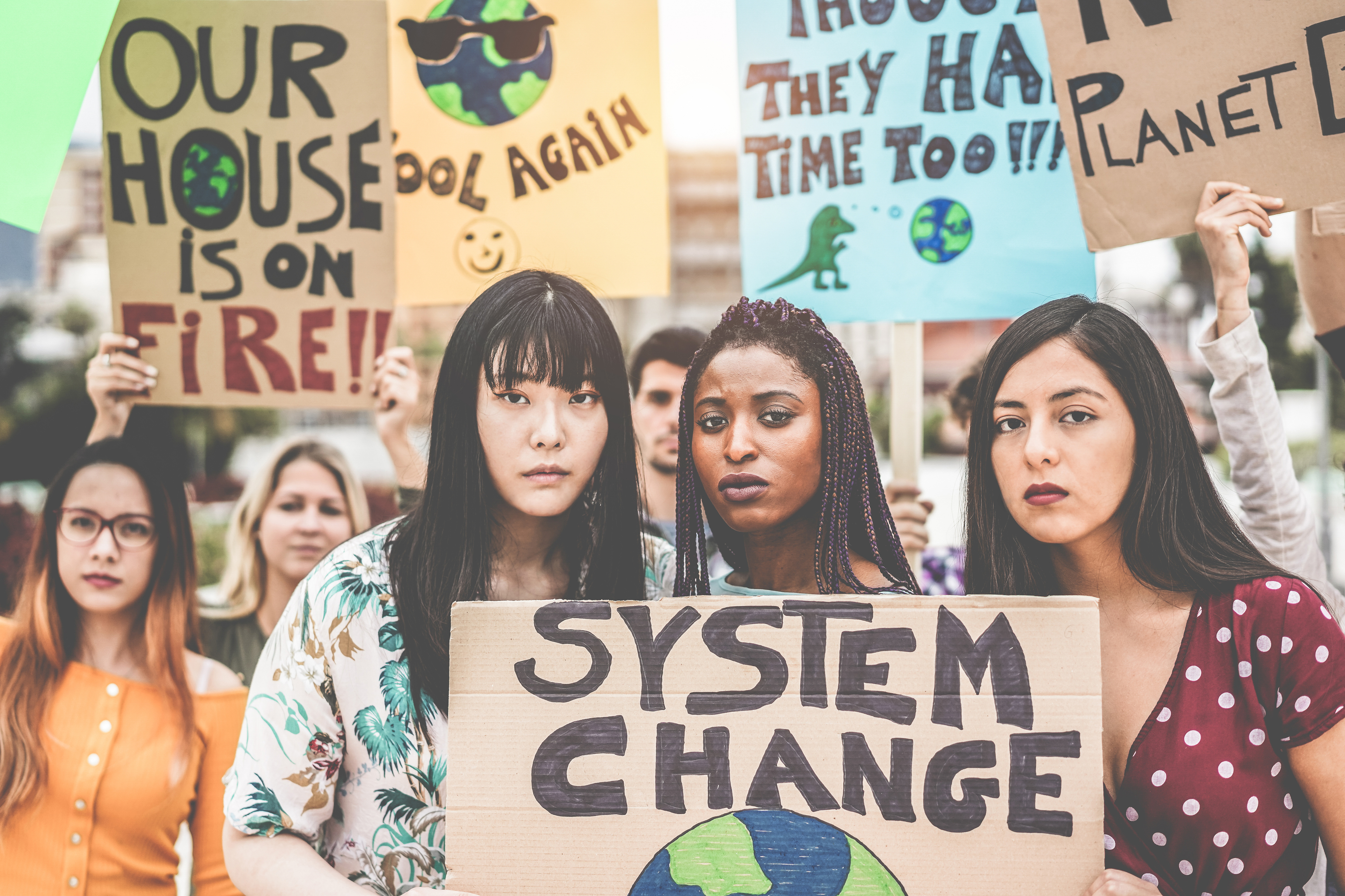 Three young people hold a sign that says "system change" as part of a protest