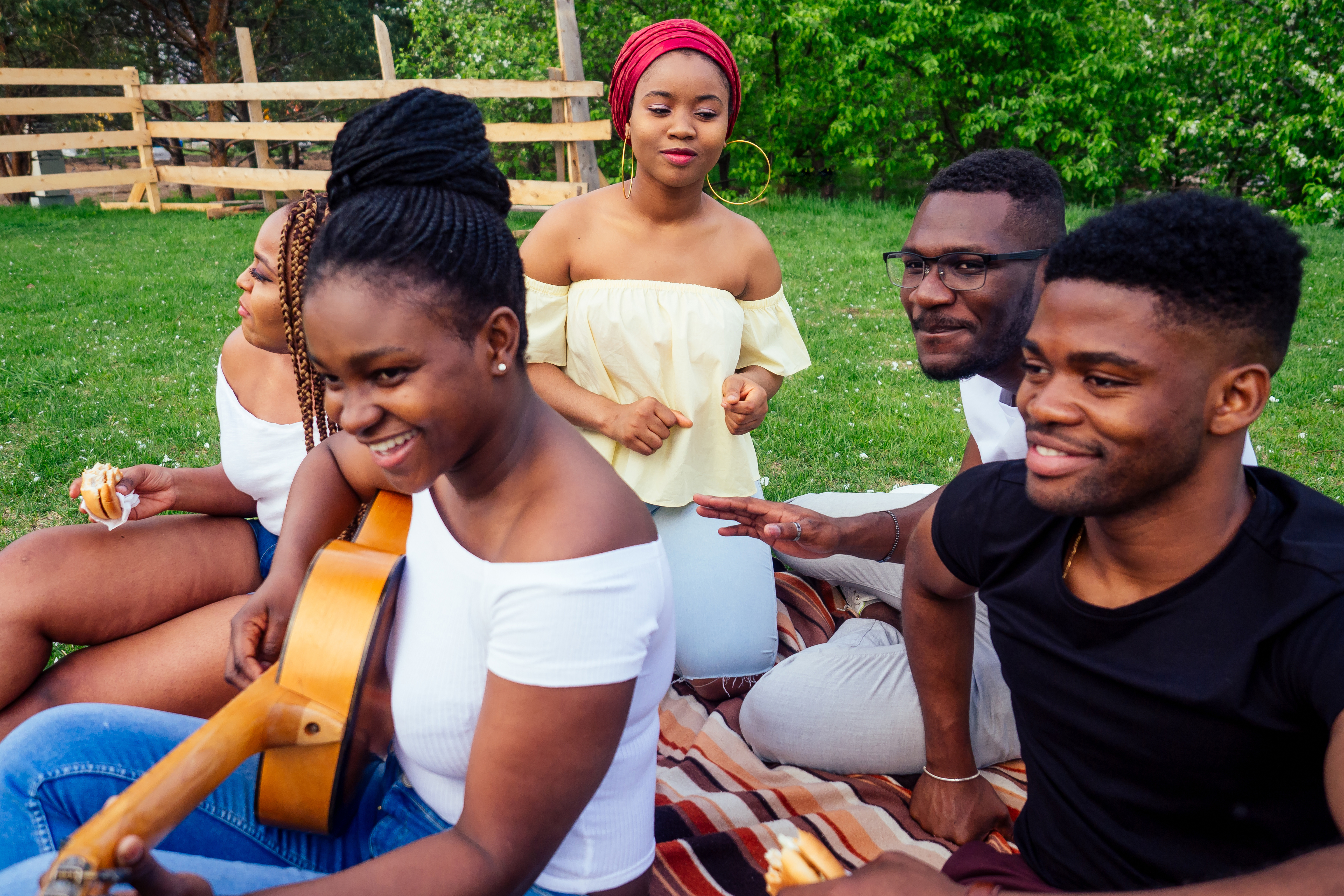 a group of teens play instruments and sit together in a park
