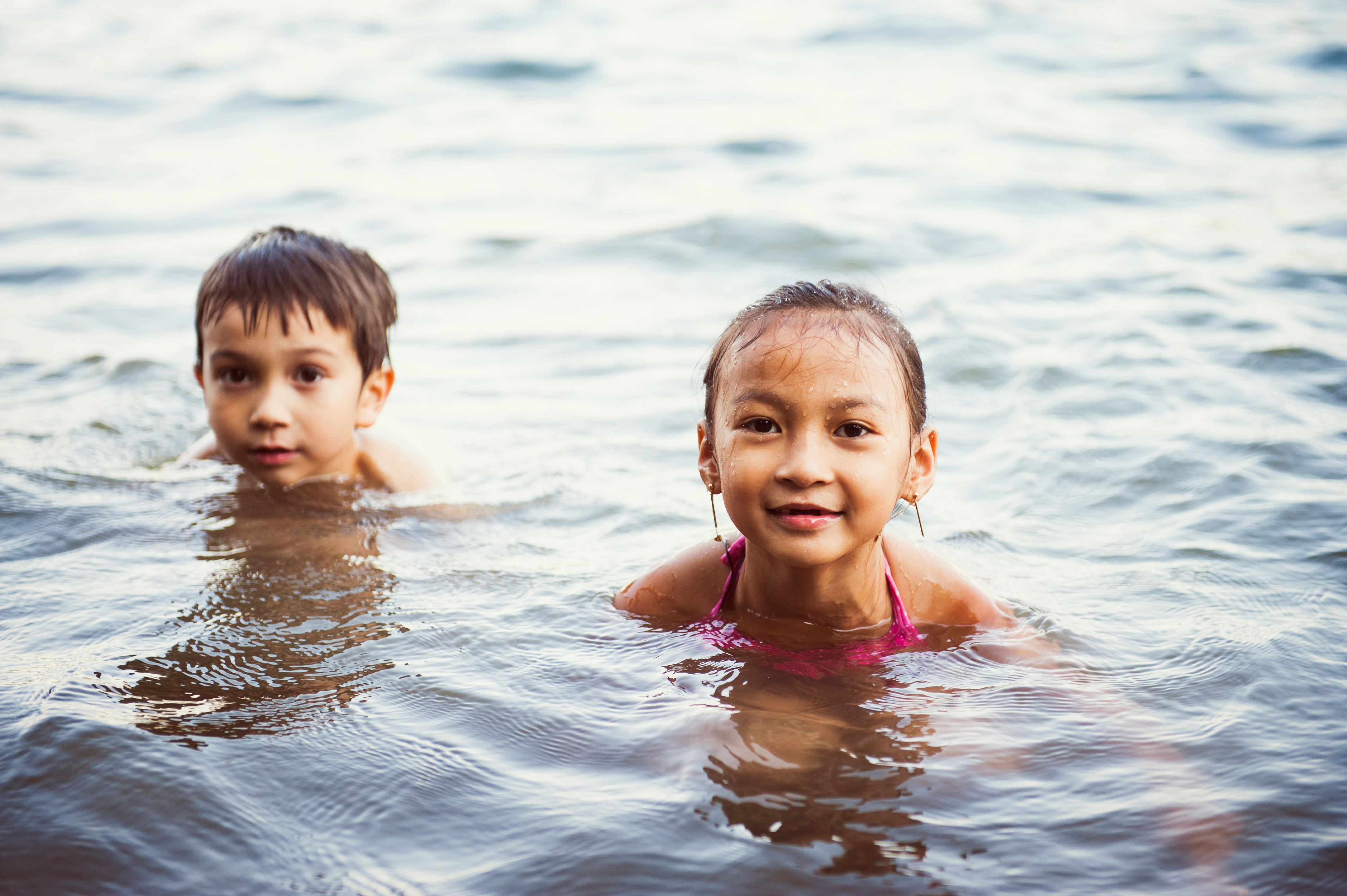 Two children swim in a lake with the heads above water