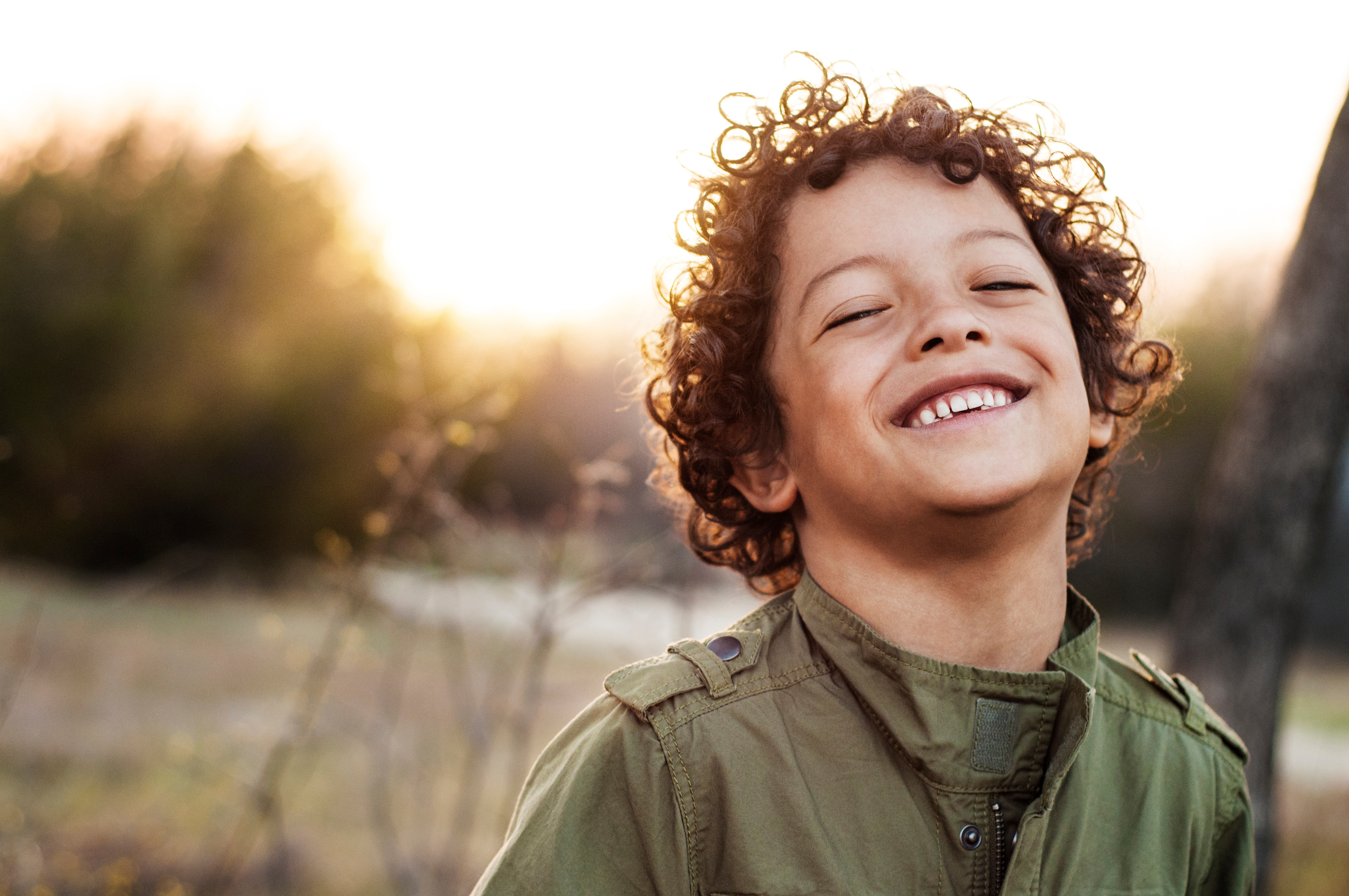 A young person smiles with their eyes closed while standing in a field