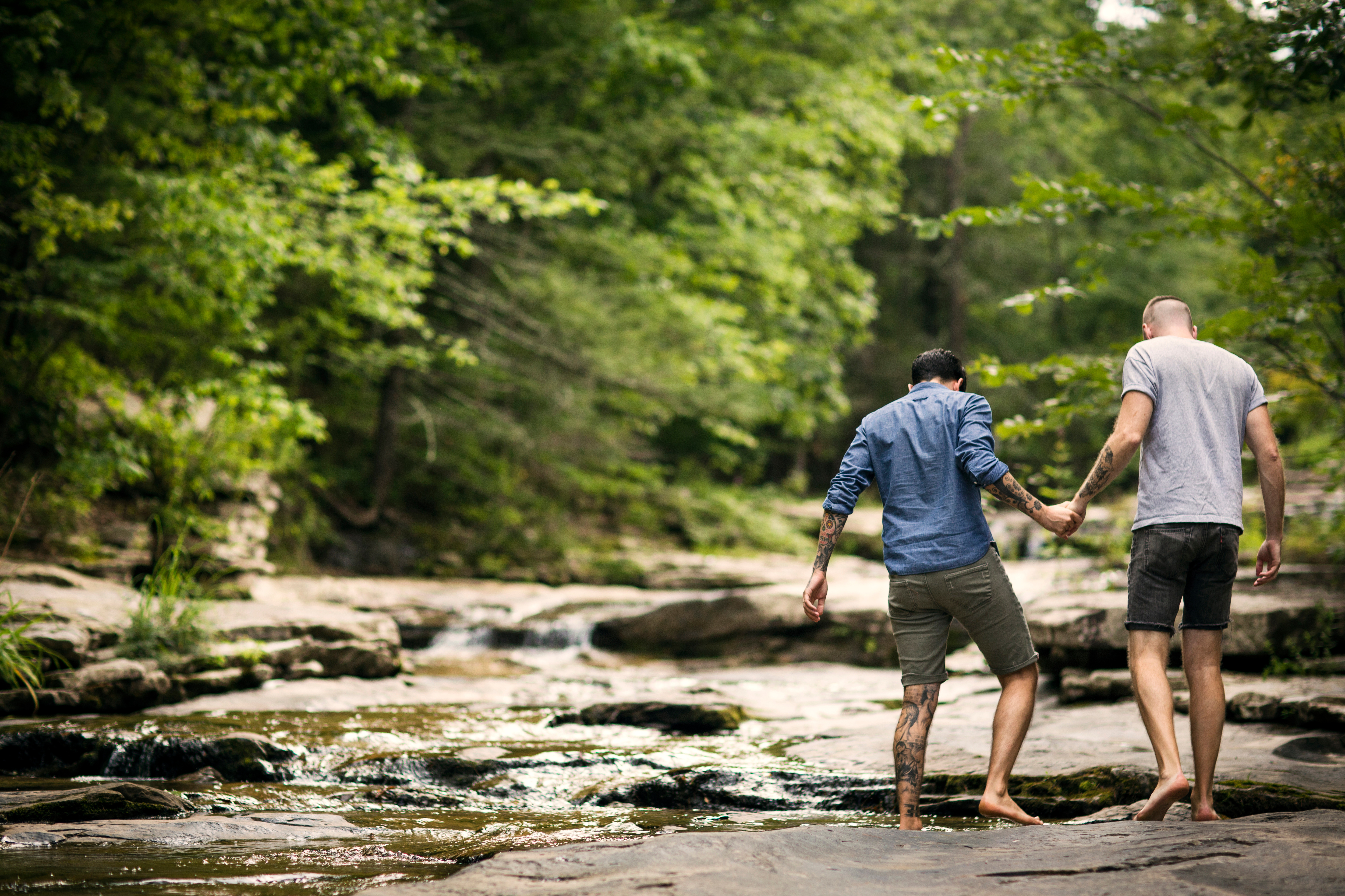 two men hold hands and step into a river in the woods