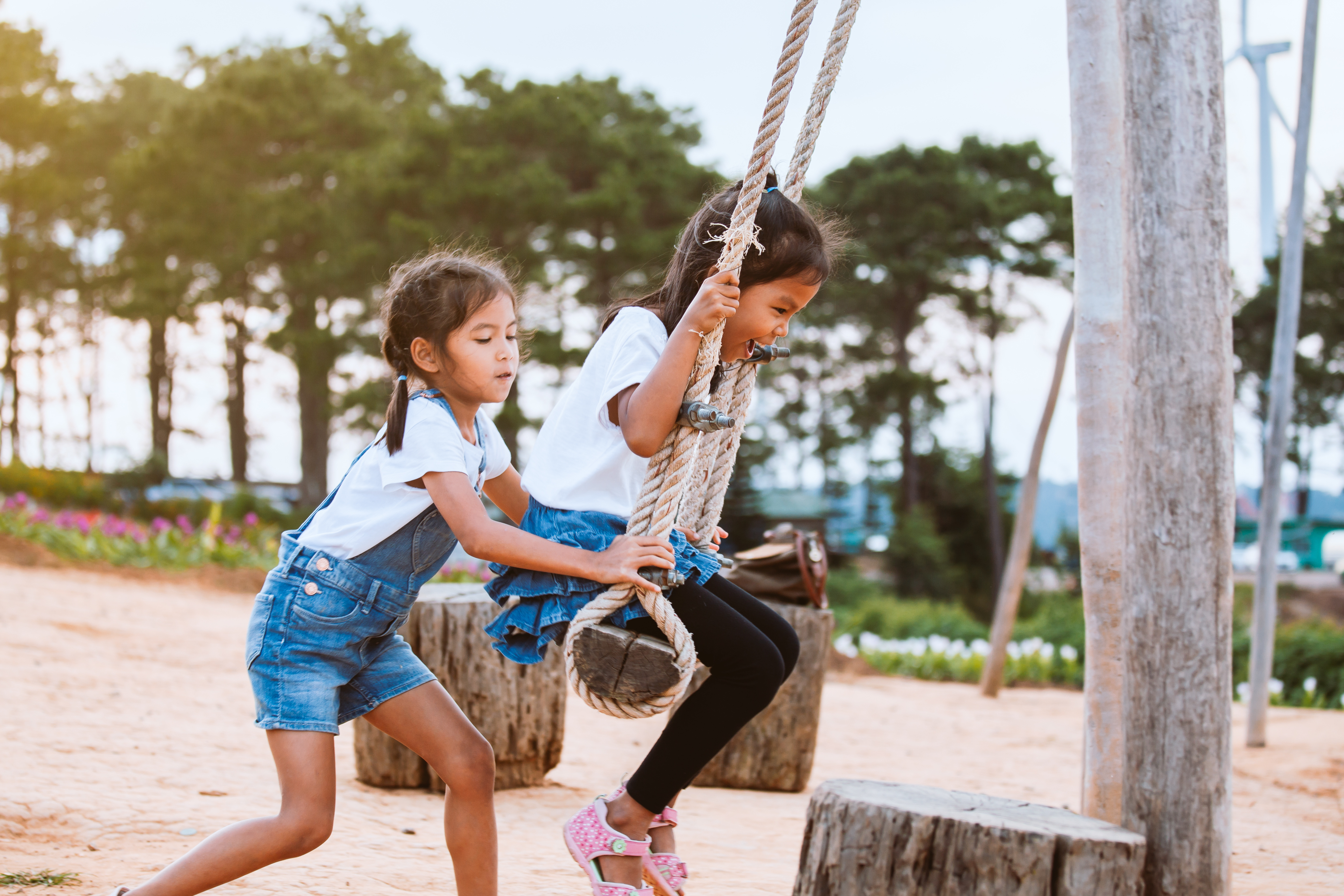 Two kids use swings on a playground