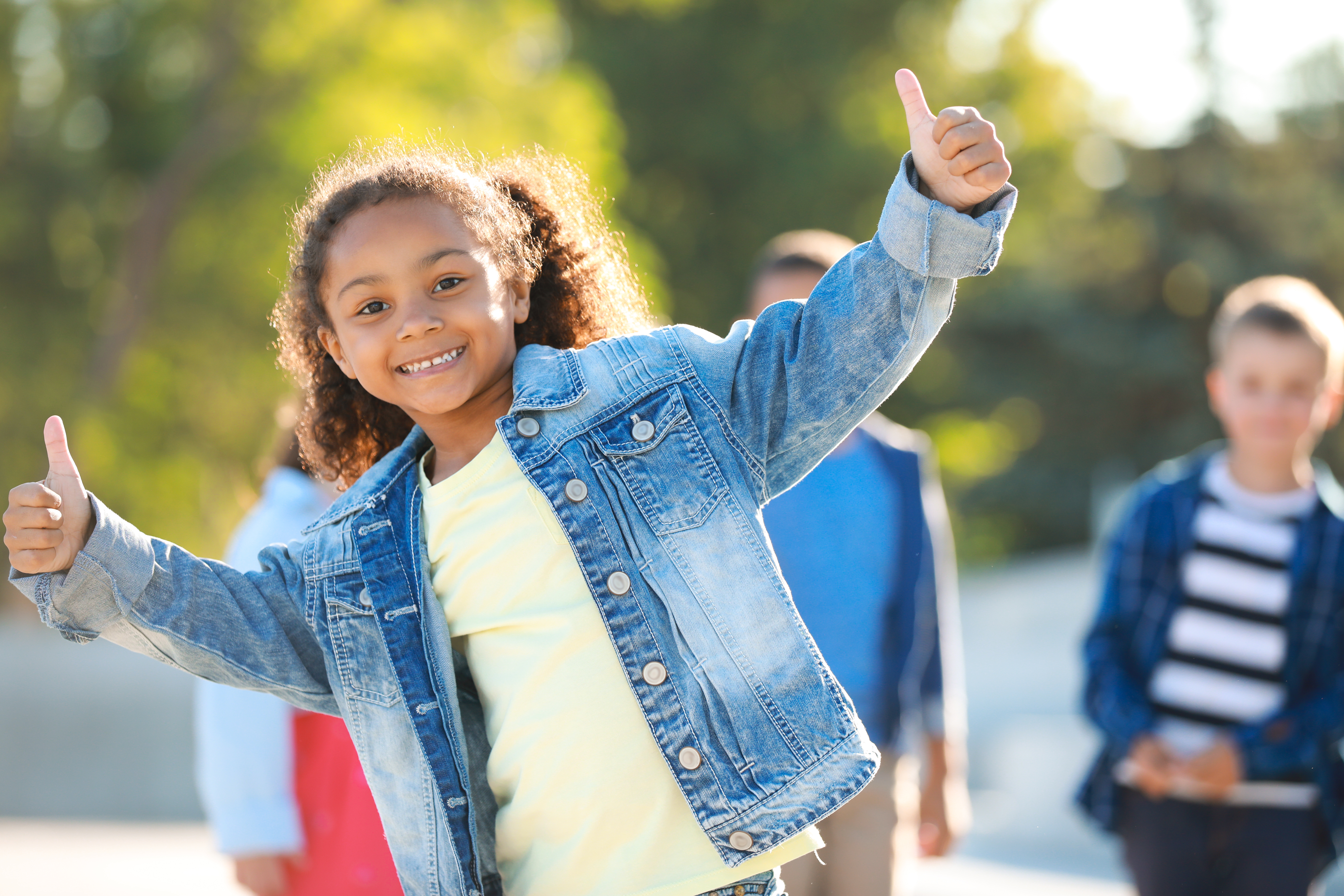 A young child smiles while holding two thumbs up