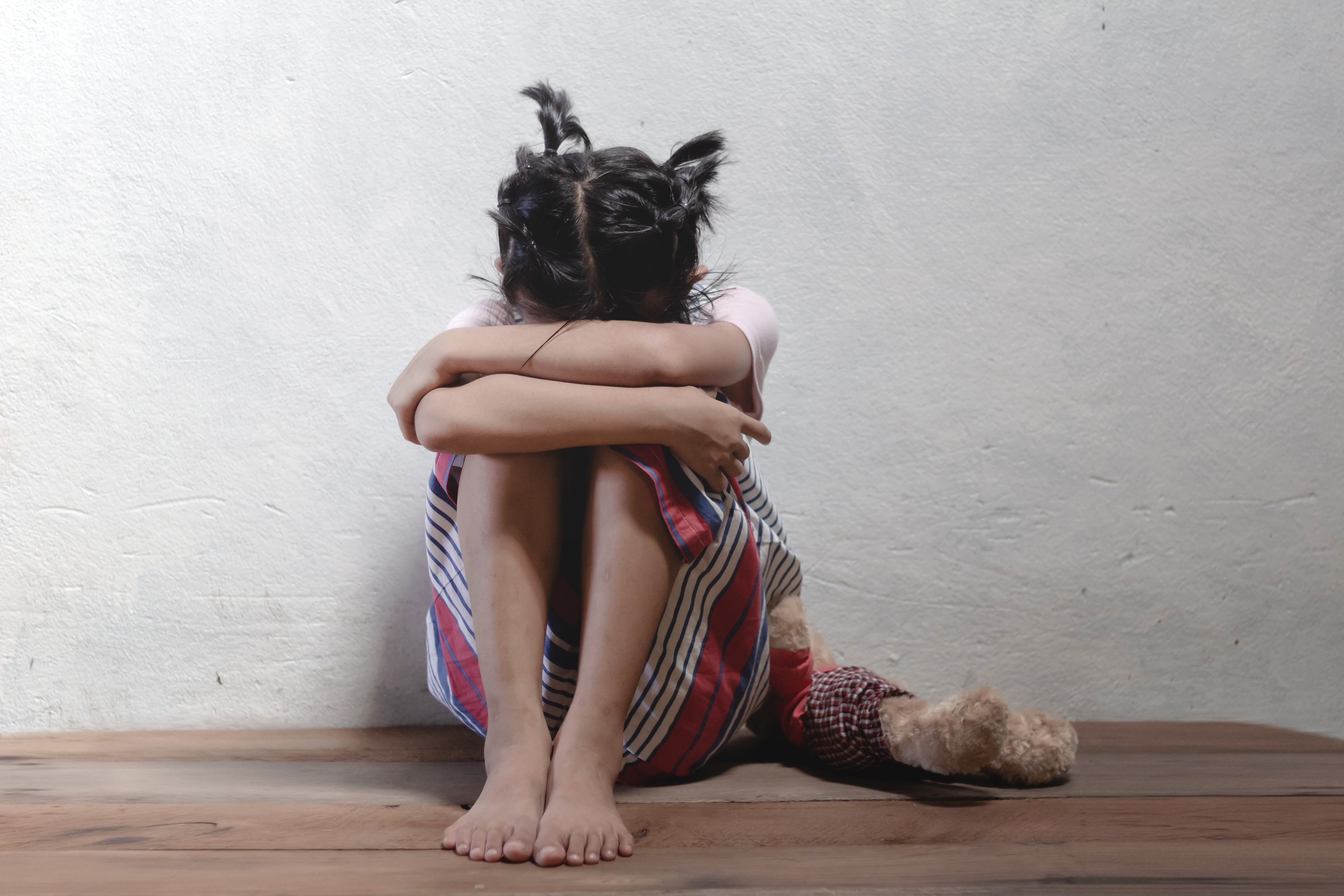 a girl sits with her head down holding a stuffed toy