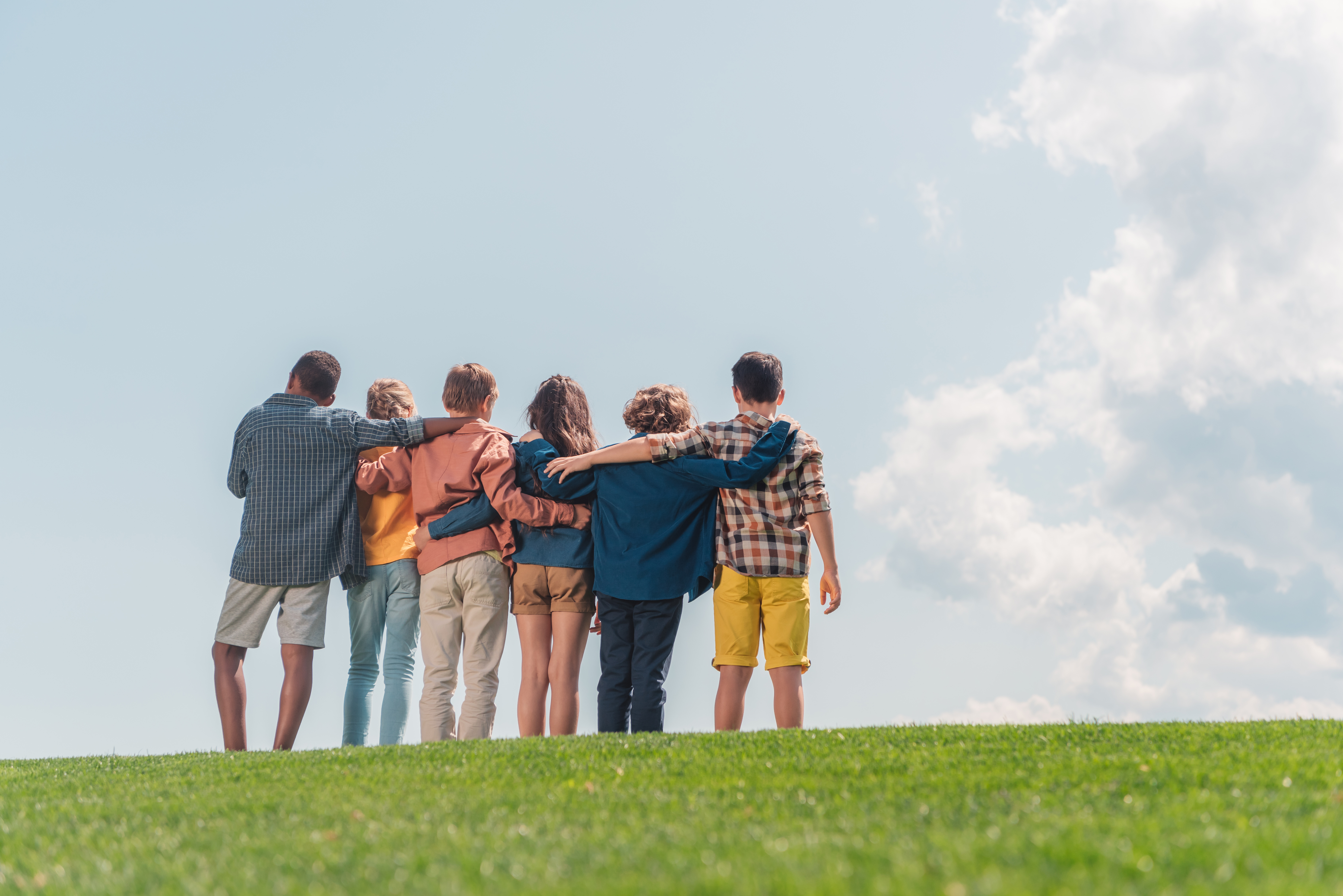A group of young people stand on a hill with their arms around each others' shoulders