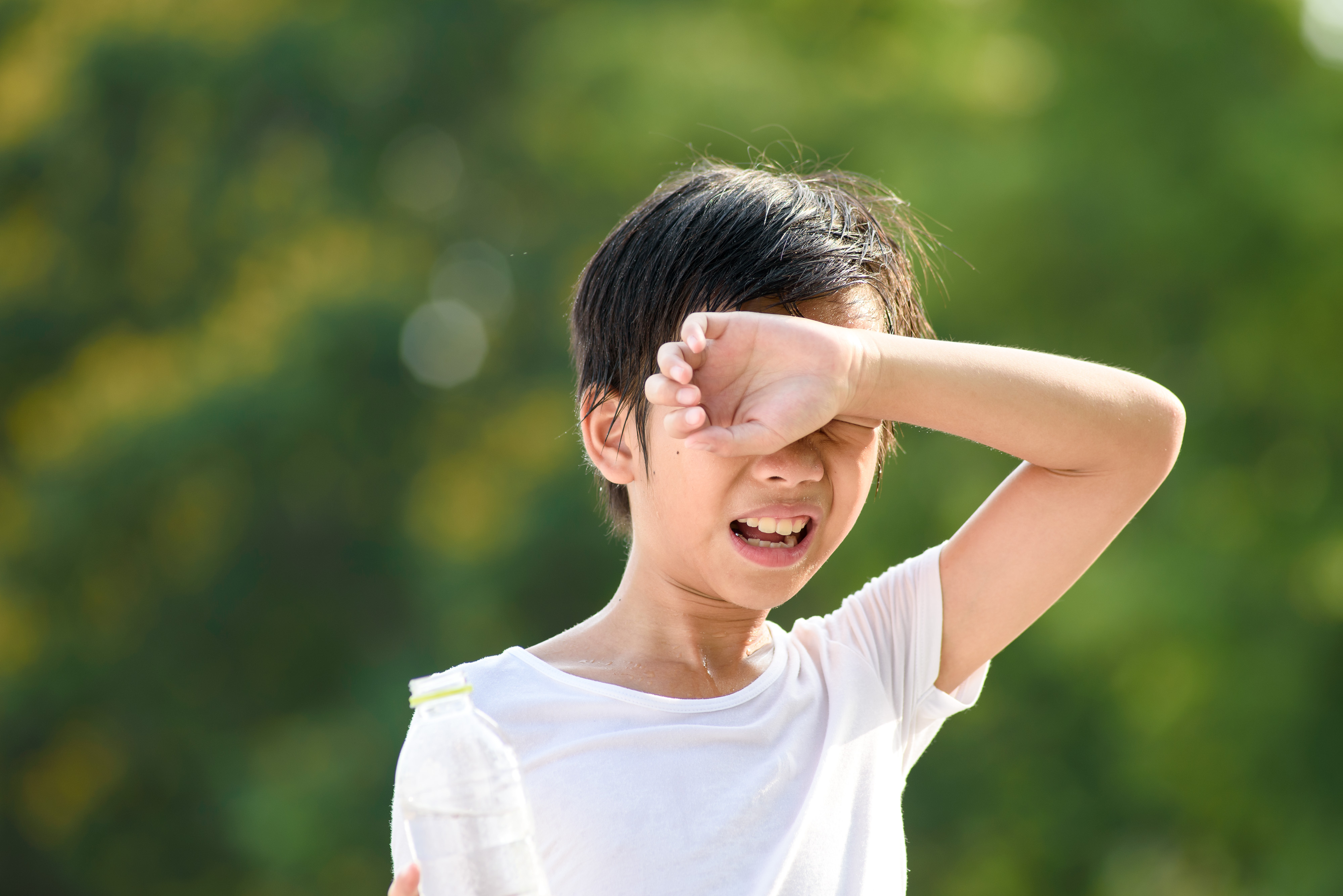 A child shades their eyes while holding a water bottle