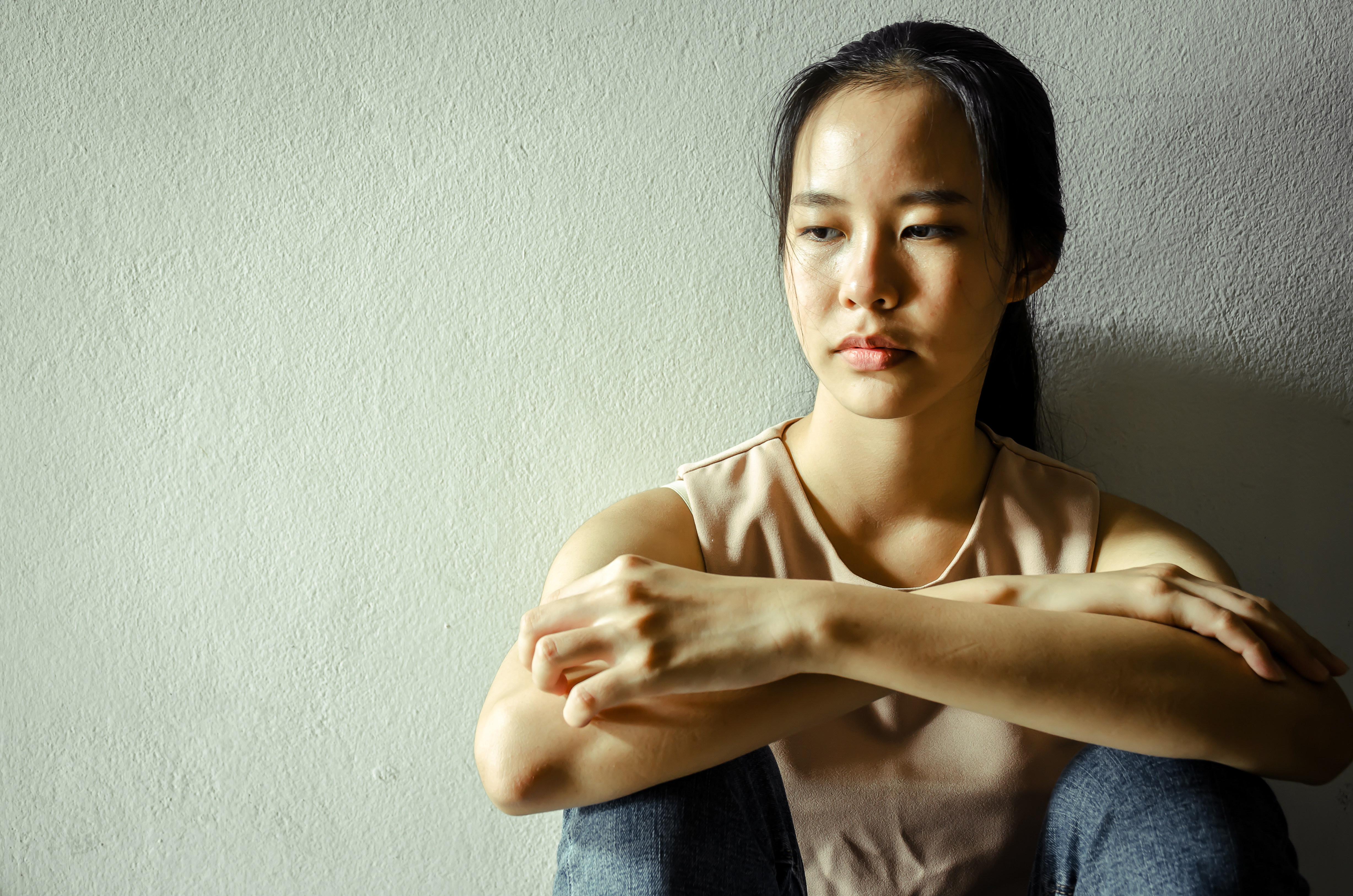 A teenage girl sits against a wall looking at the ground