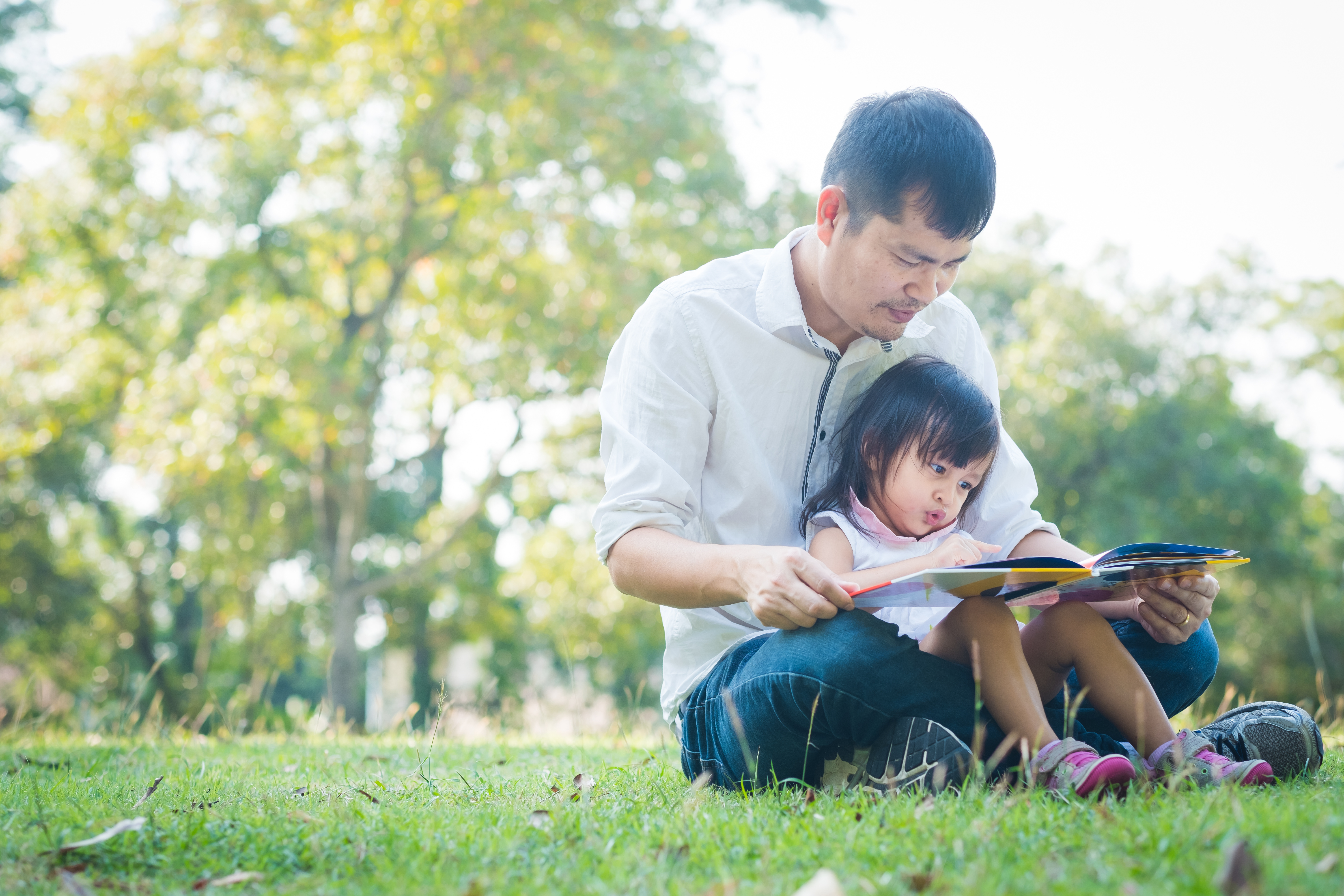 A man and child sit together outside looking at a book
