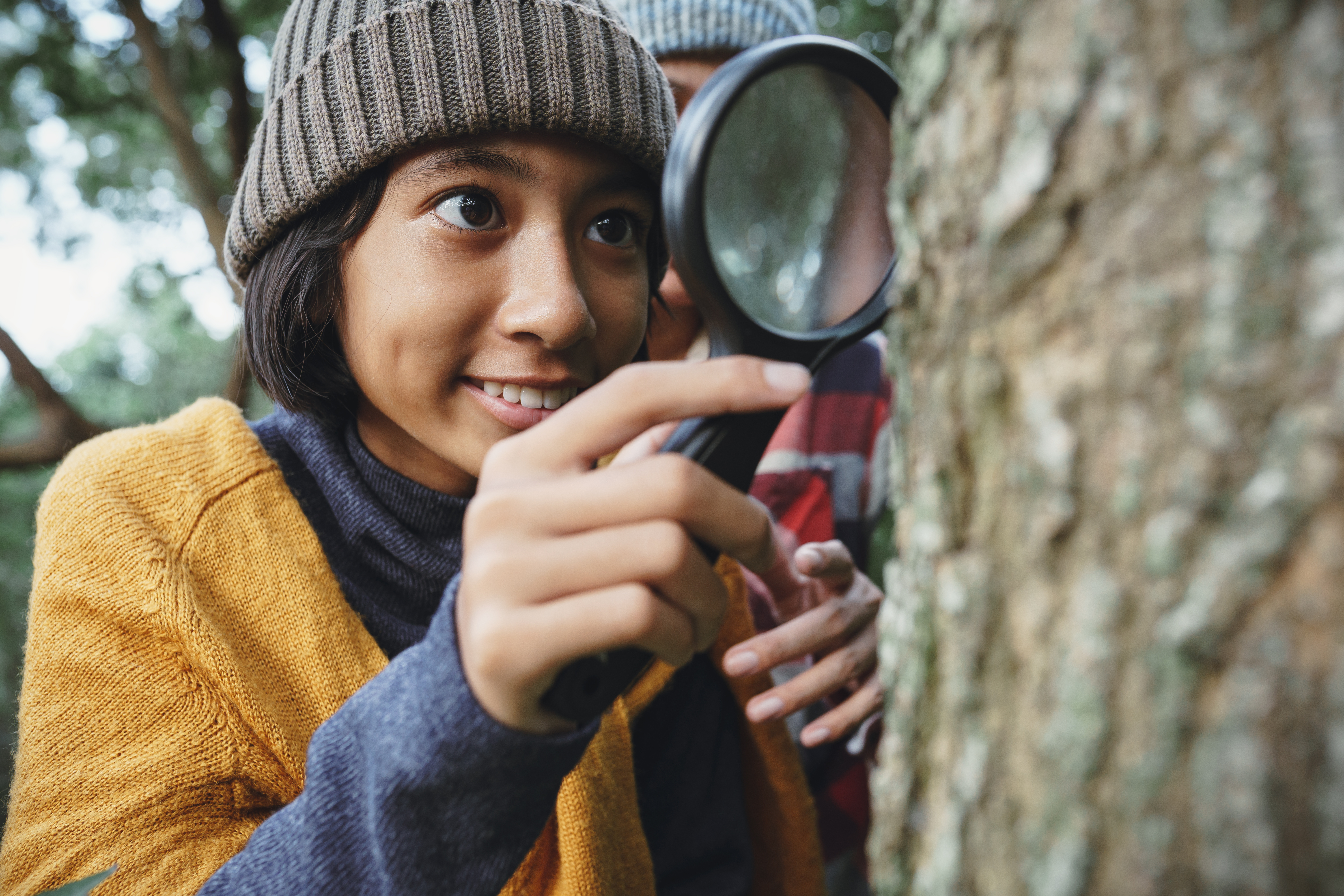 A young person examines a tree with a magnifying glass
