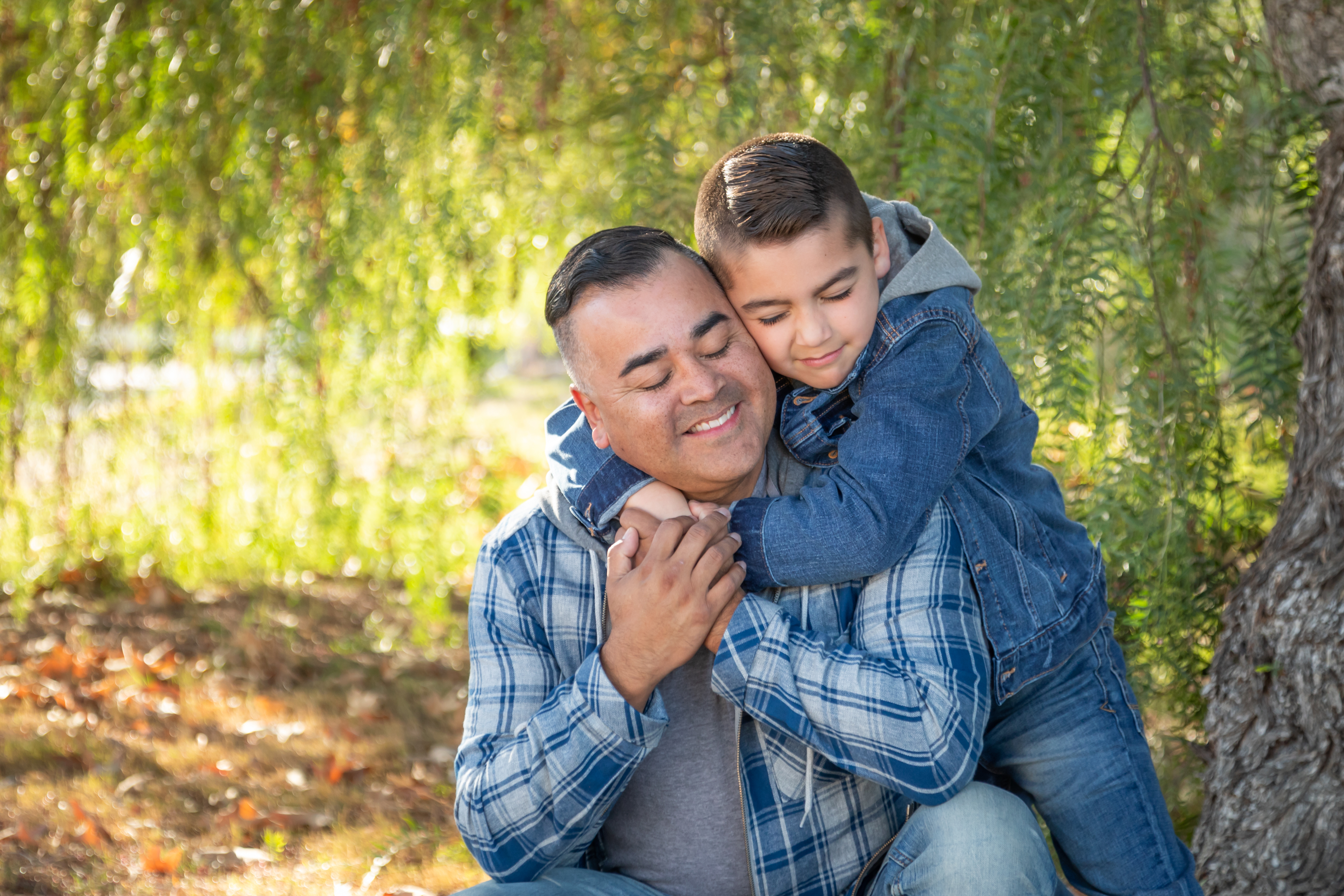 A child hugs an adult around the shoulders while standing under a tree