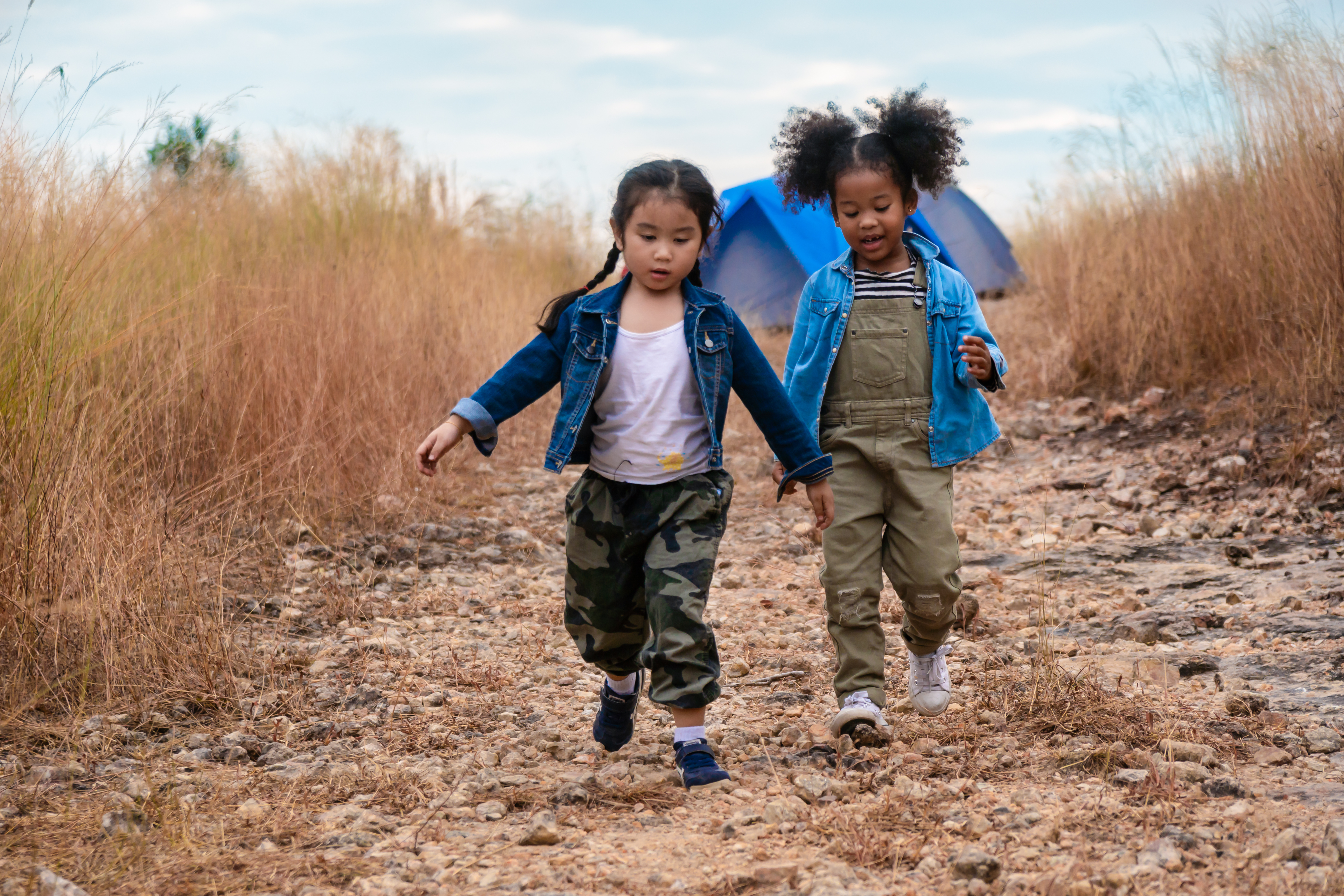 young girls walk near a tent in a field