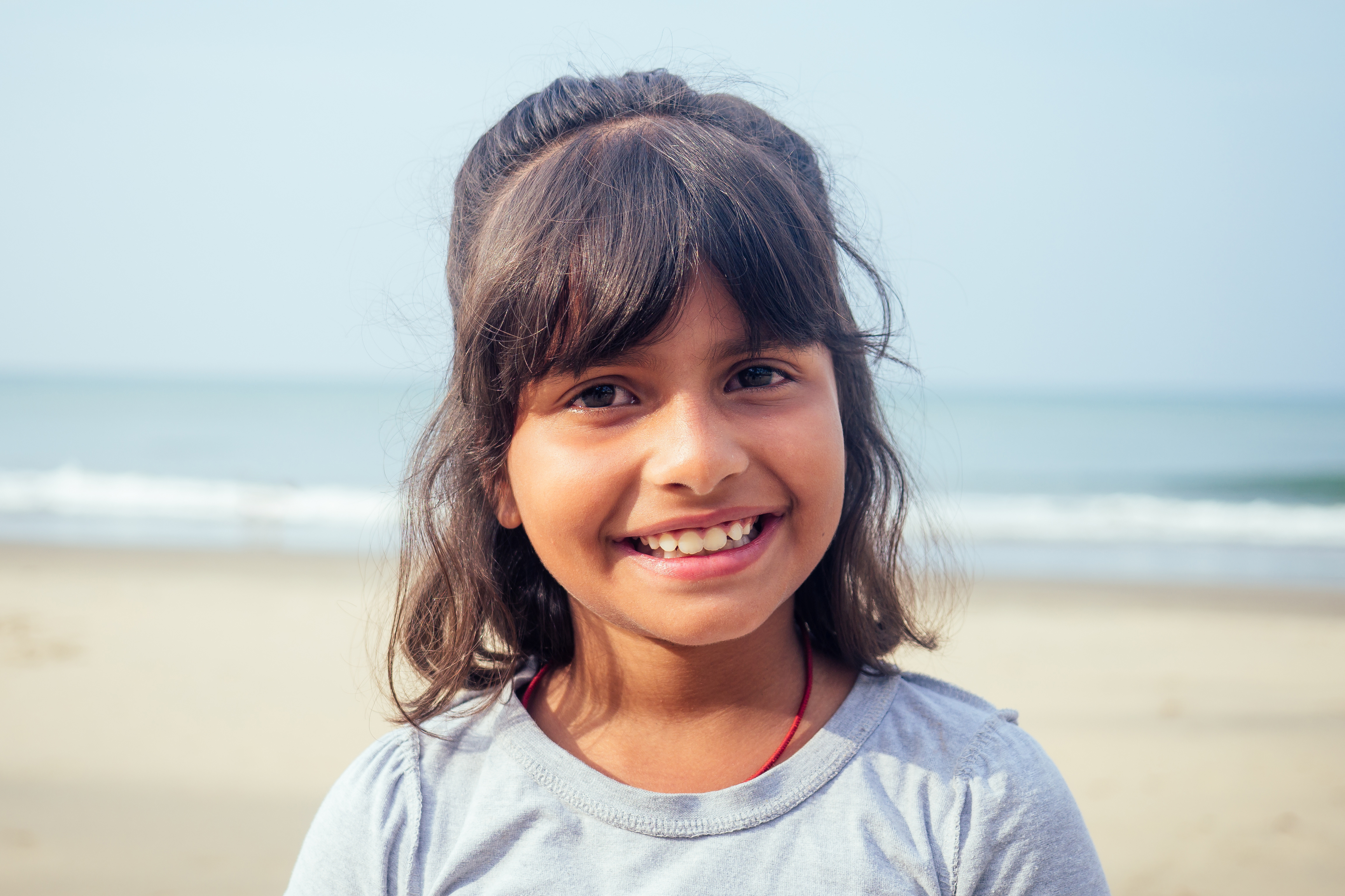 A young child stands on the beach staring at the camera. 