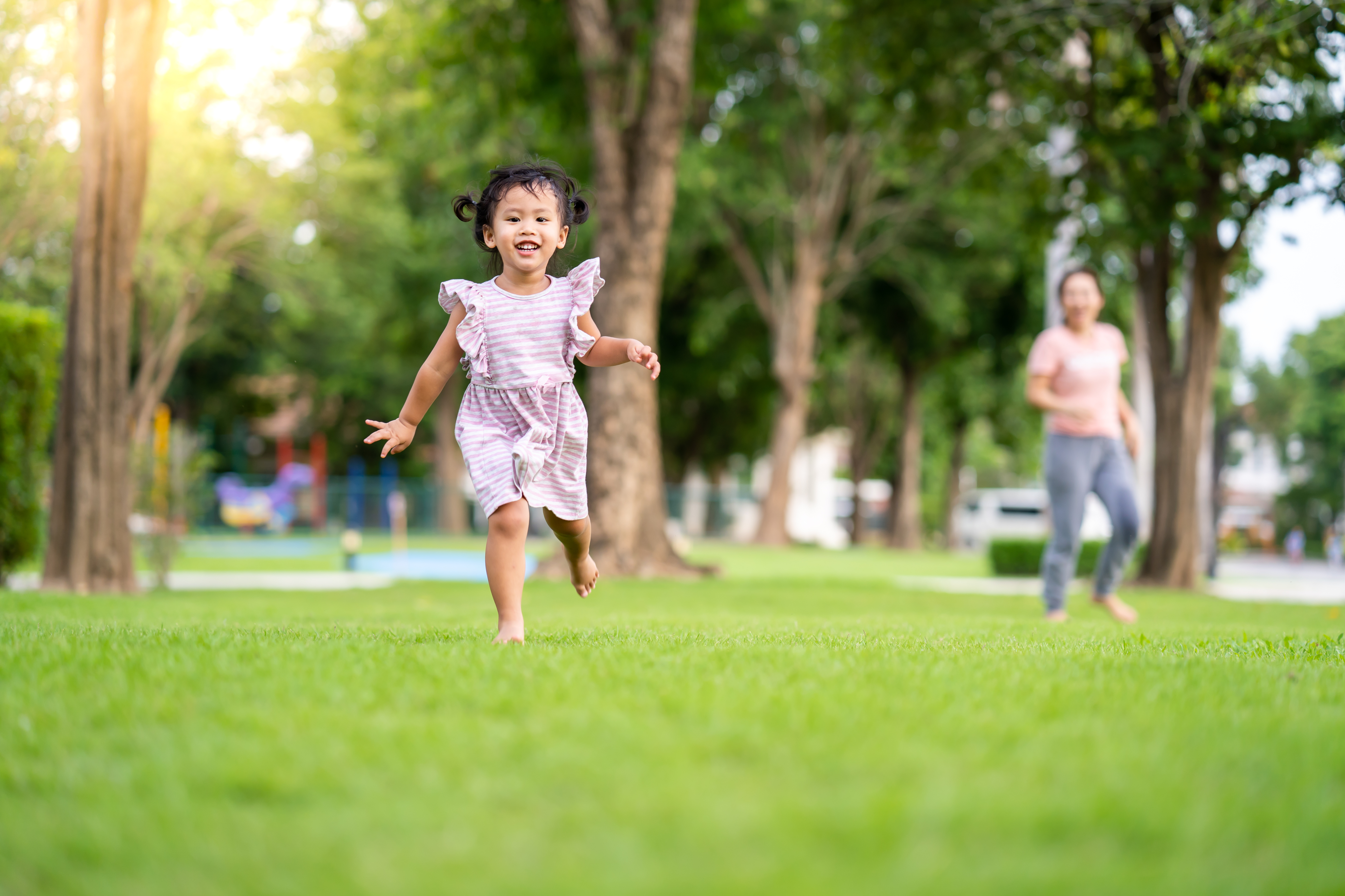 a child runs across a lawn at the park in a pink dress
