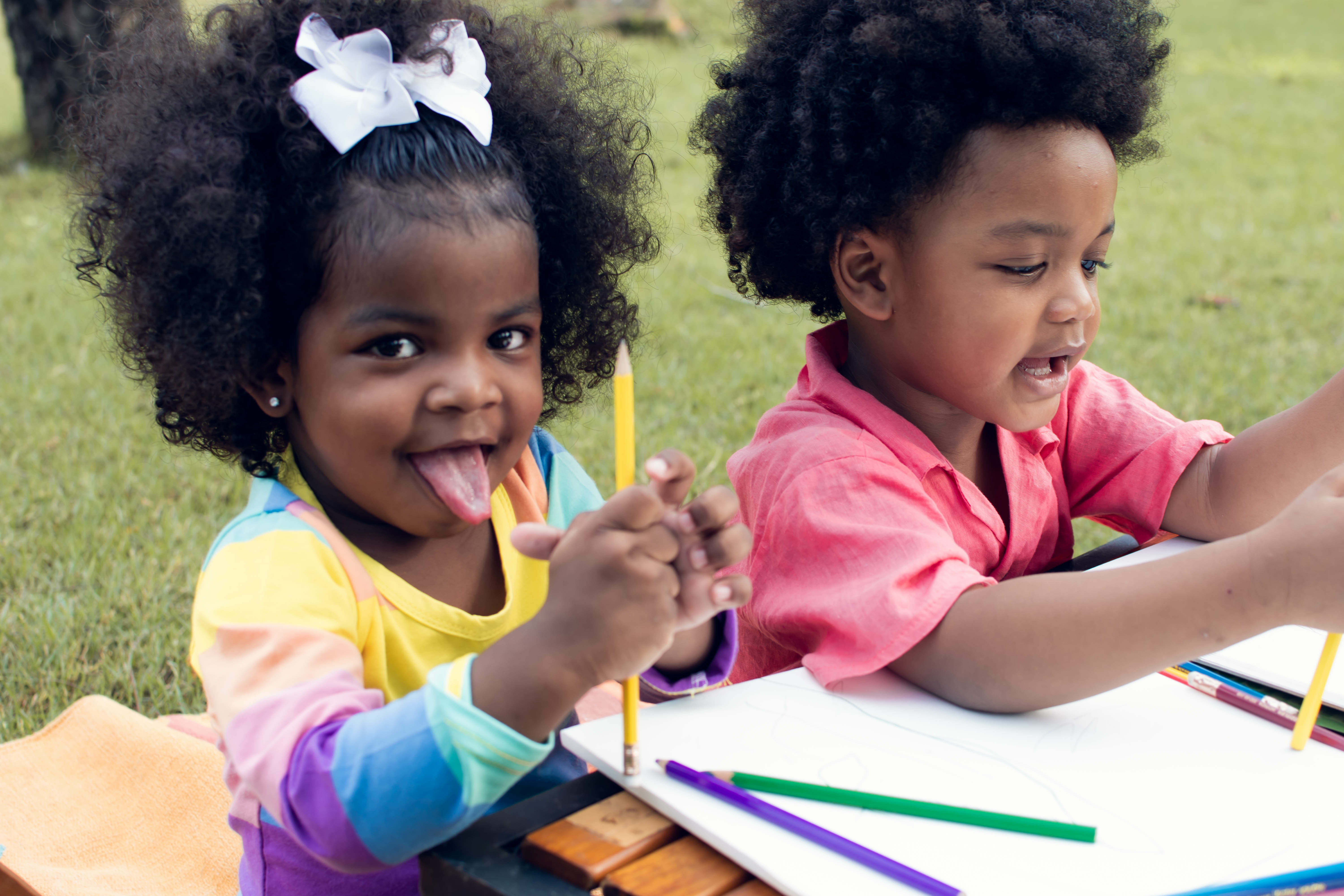 two kids hold art supplies while sitting outside