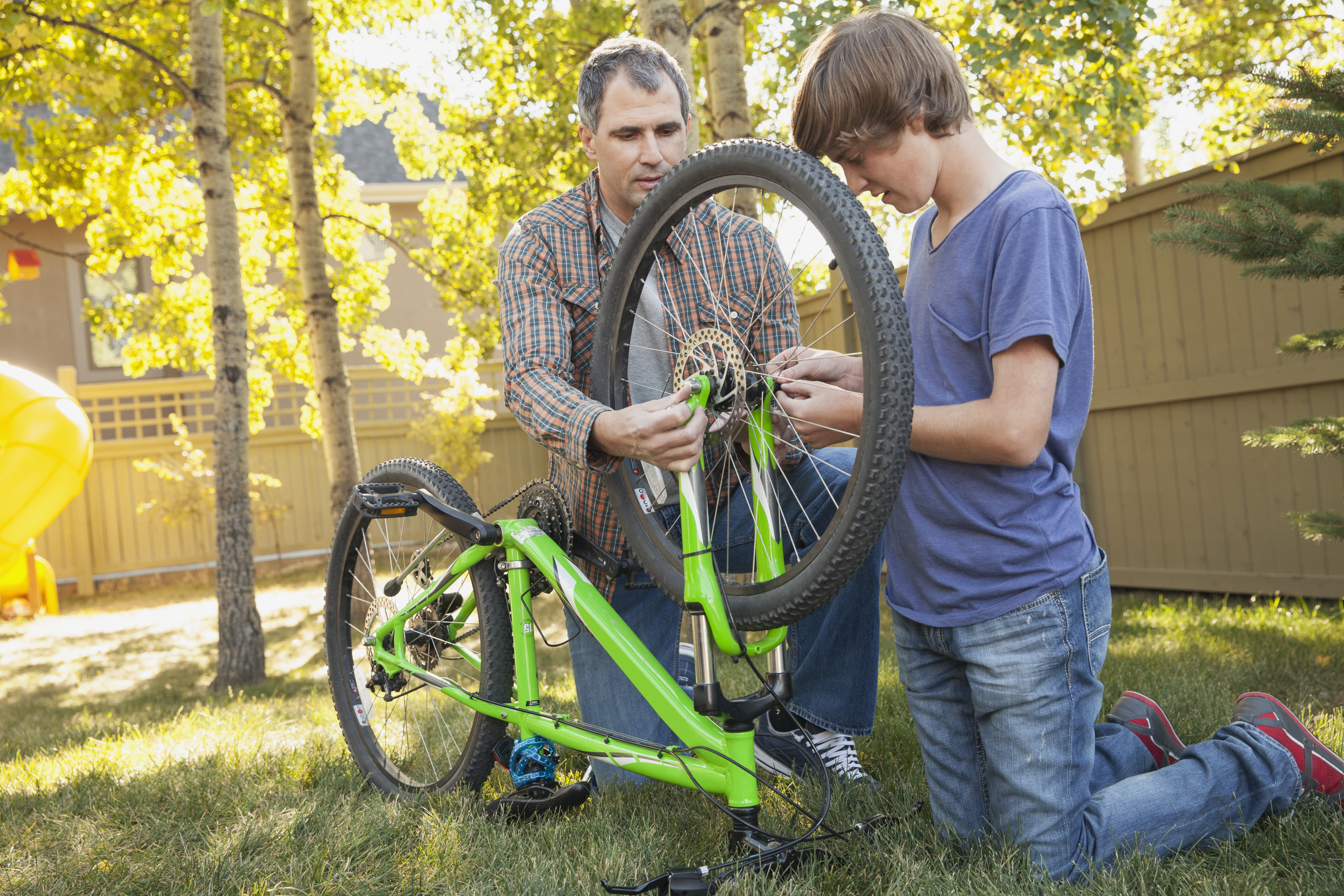 teen boy and dad working on a bike in backyard