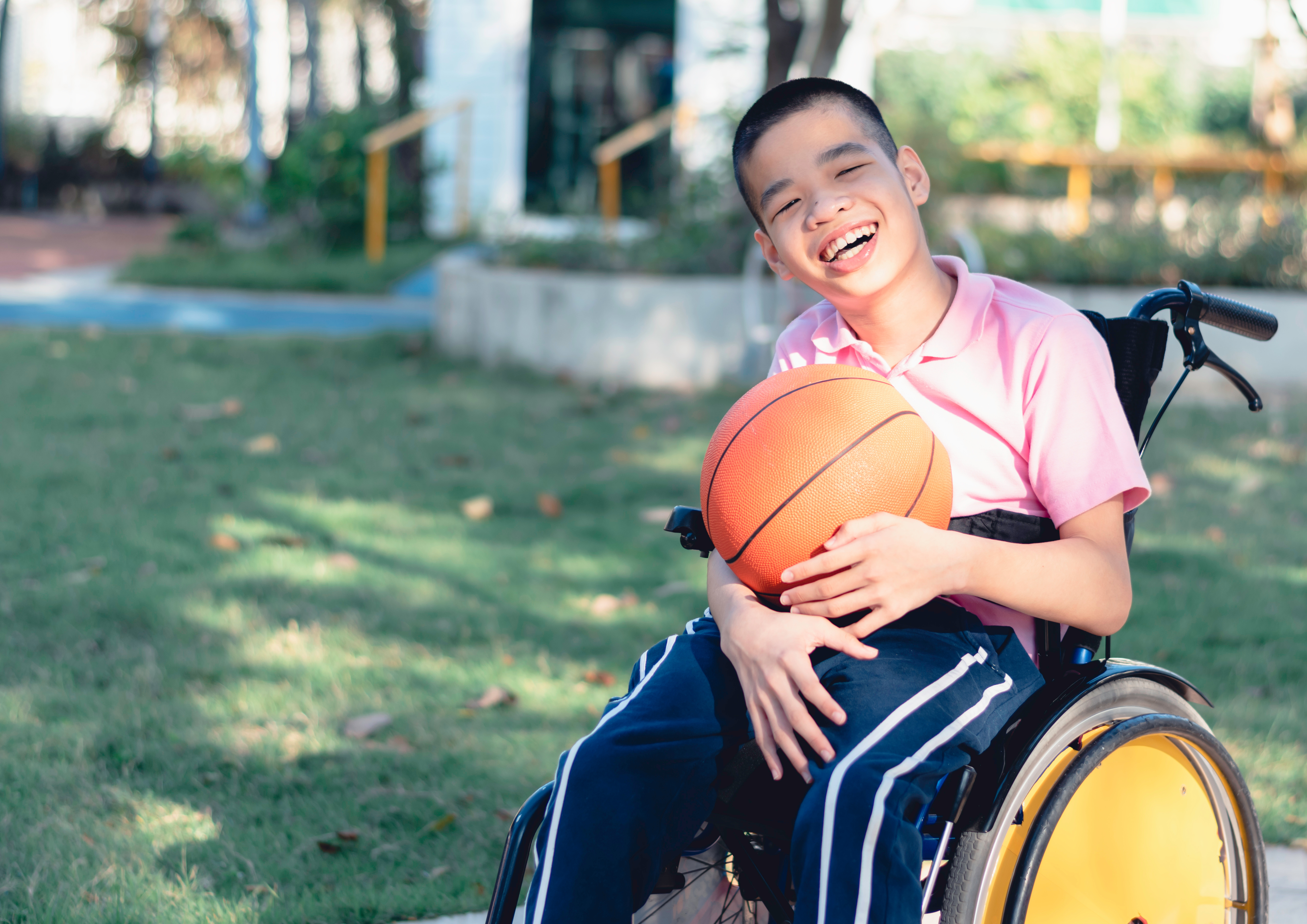 A boy holds a basketball while sitting in a wheelchair