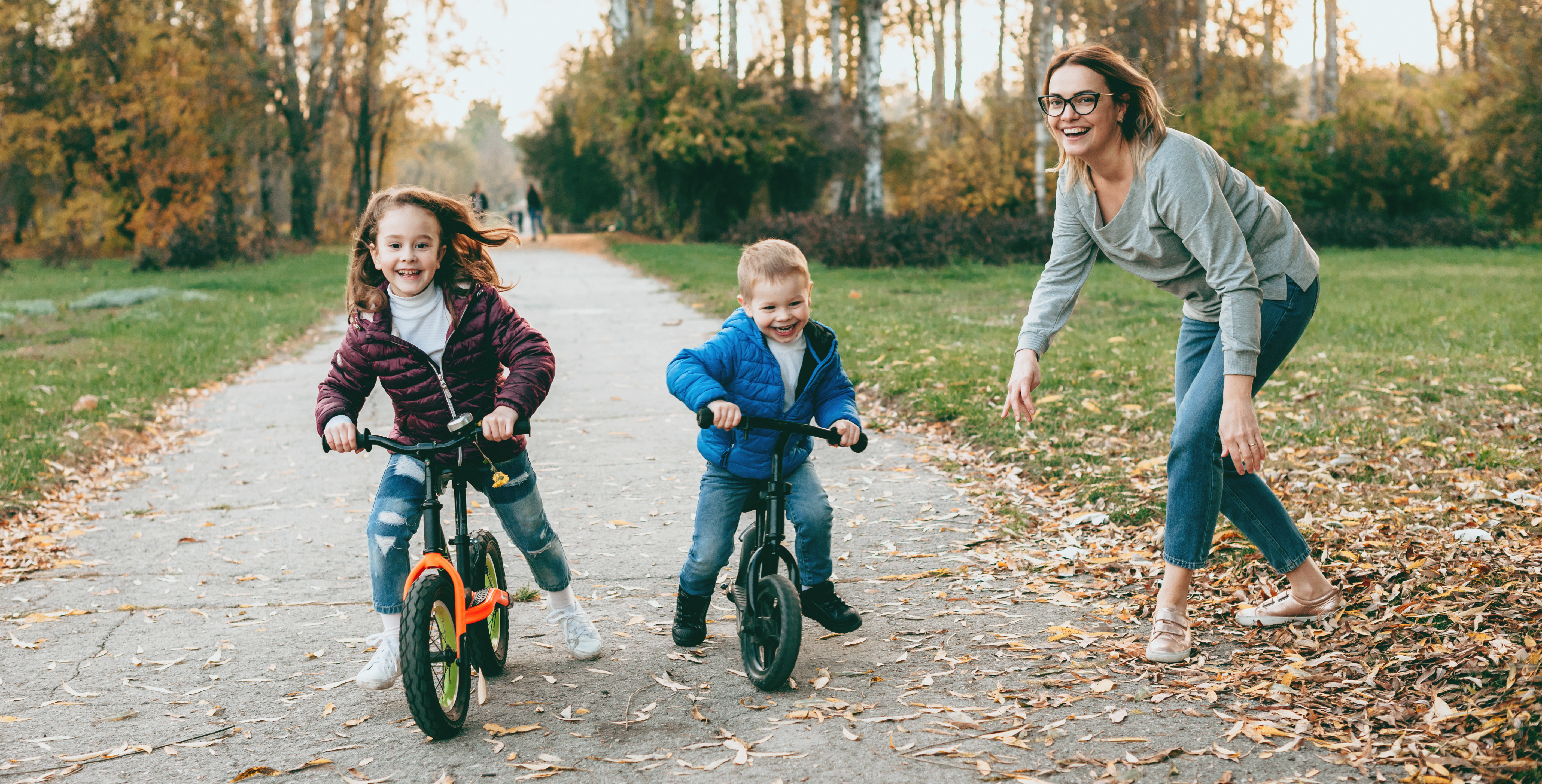 a parent and two young children ride bikes on a greenway