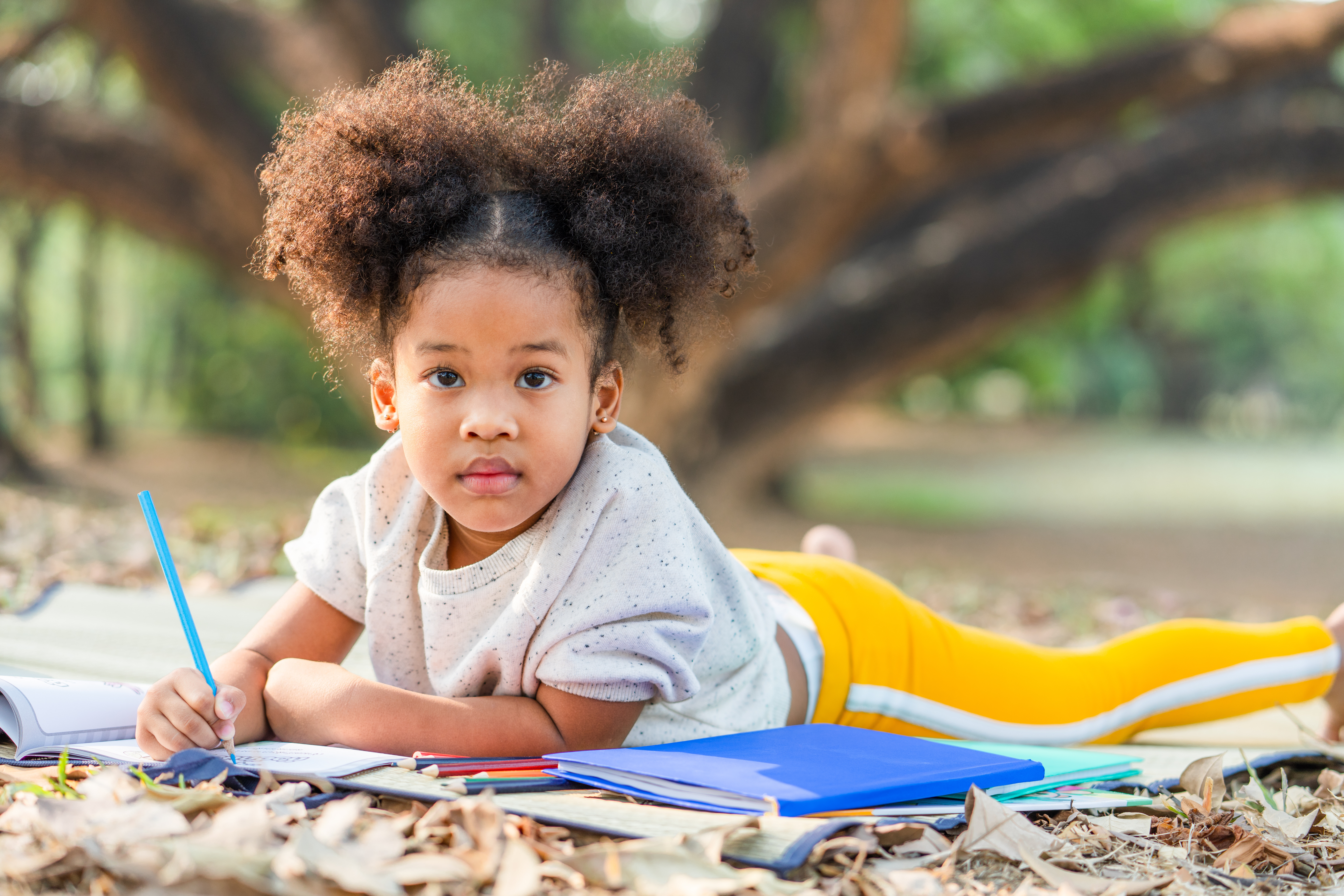 A young child stares at the camera while laying on the ground writing