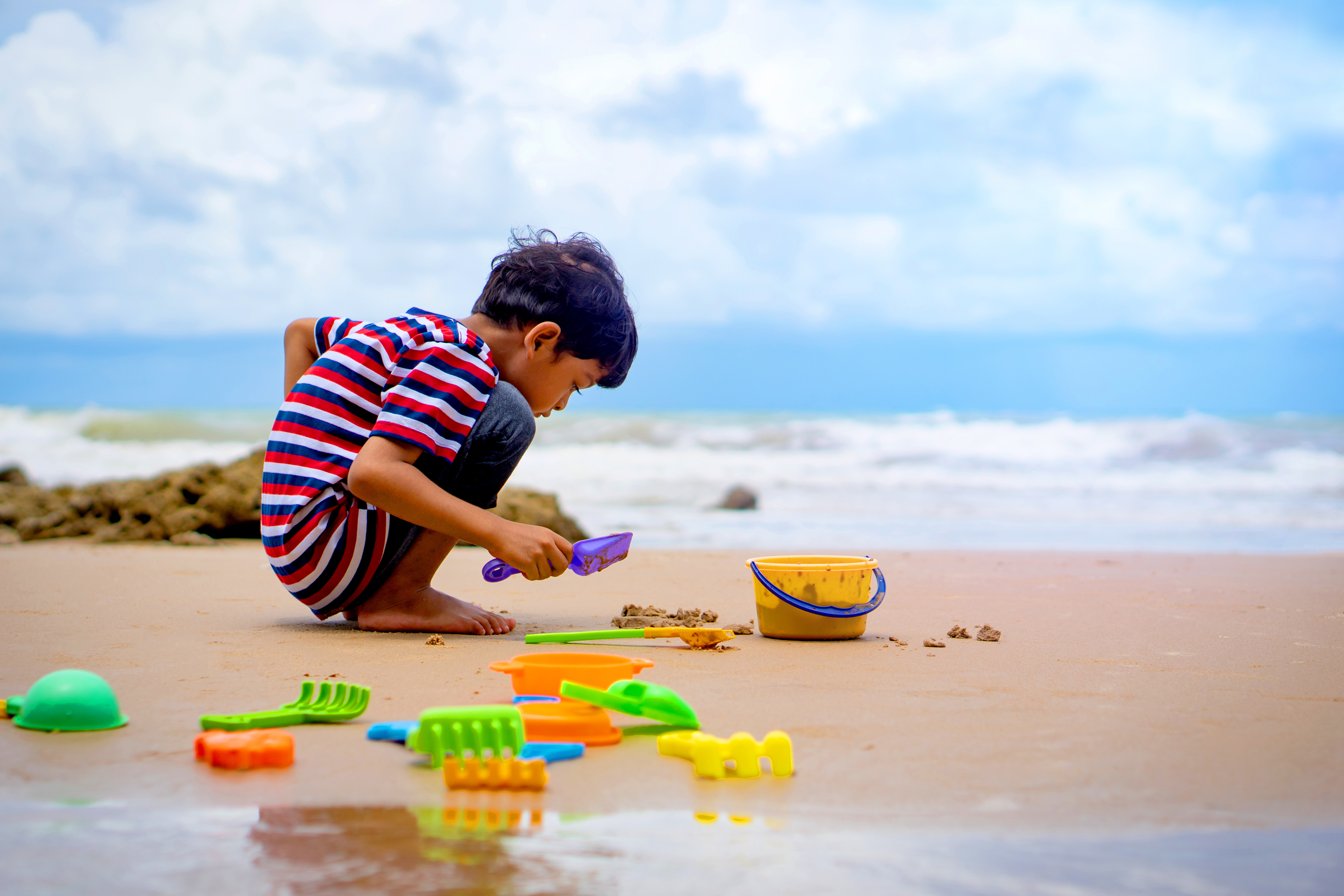 A boy plays on the beach with the ocean behind him