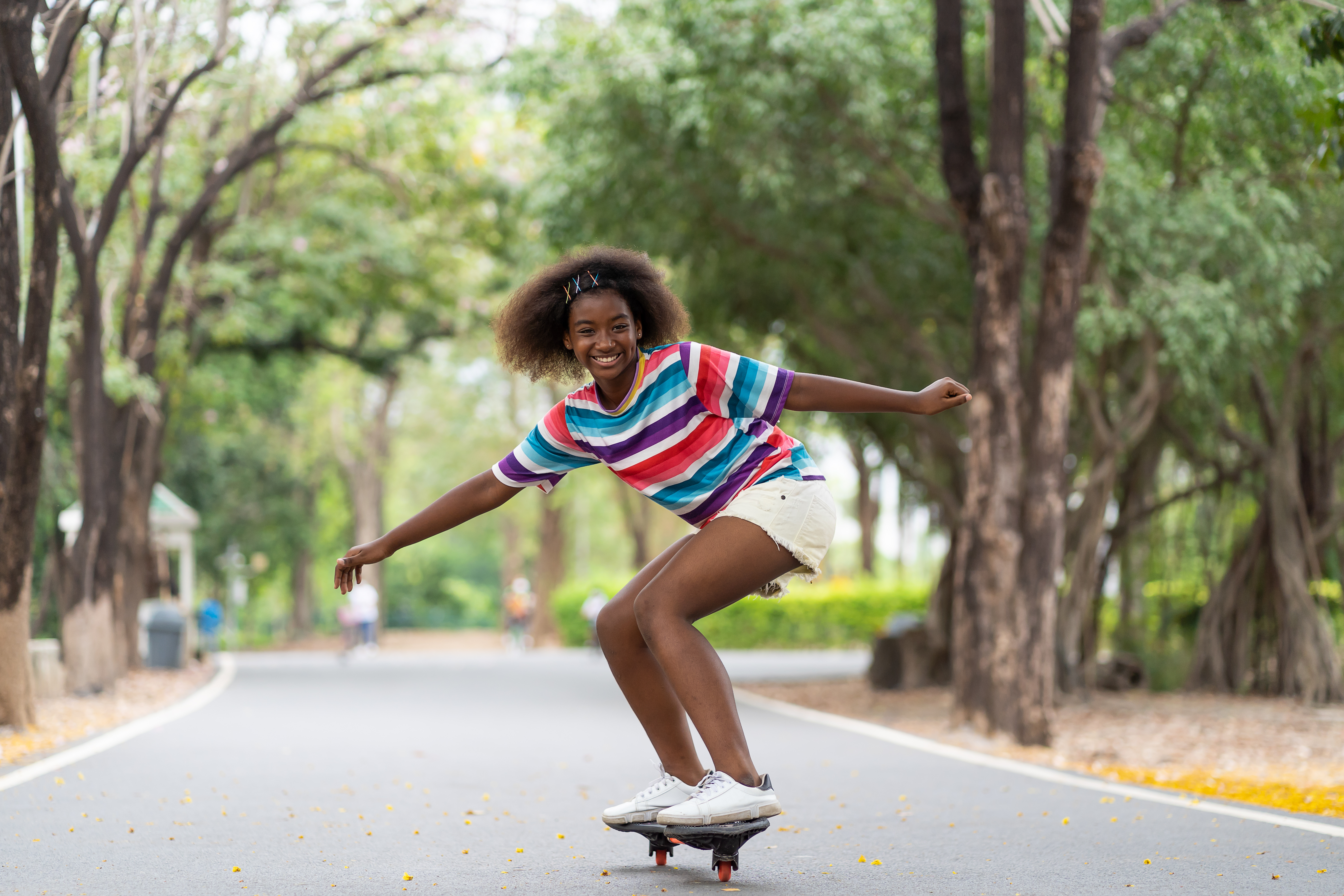 A teenager rides a skateboard through a line of trees