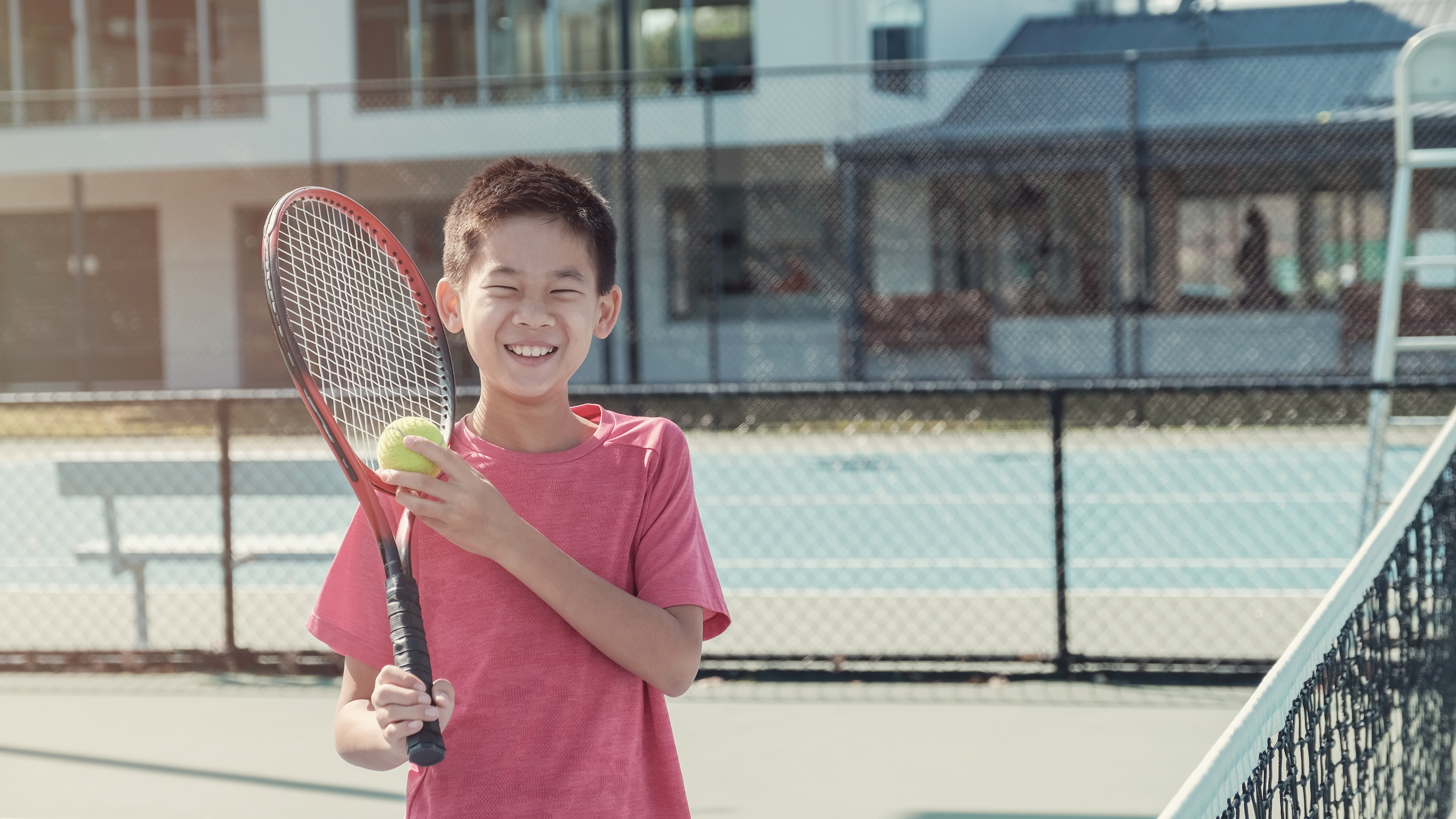 a boy stands on a tennis court with a racket and ball