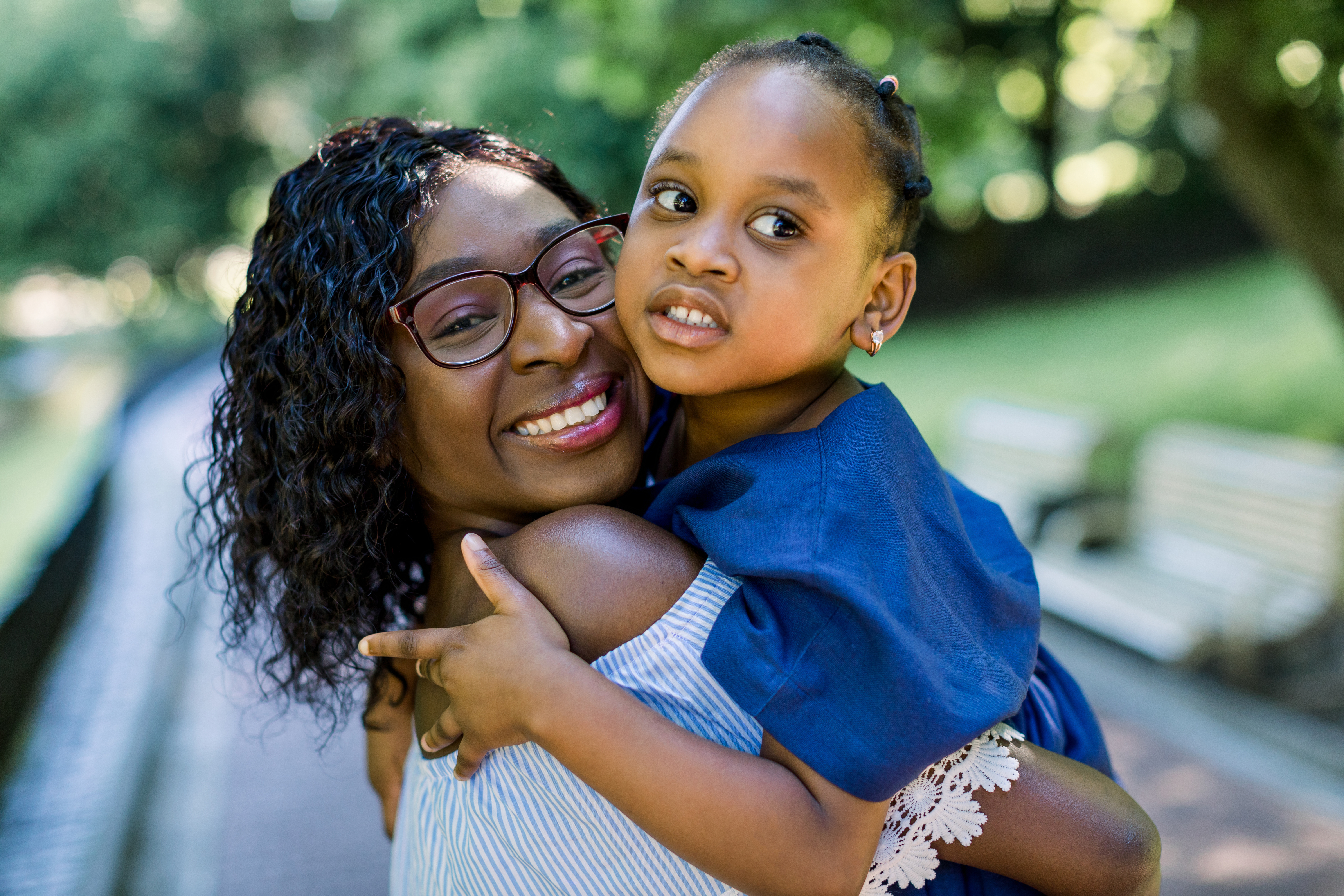 A woman holds a little girl in her arms in front of a tree and smiles.