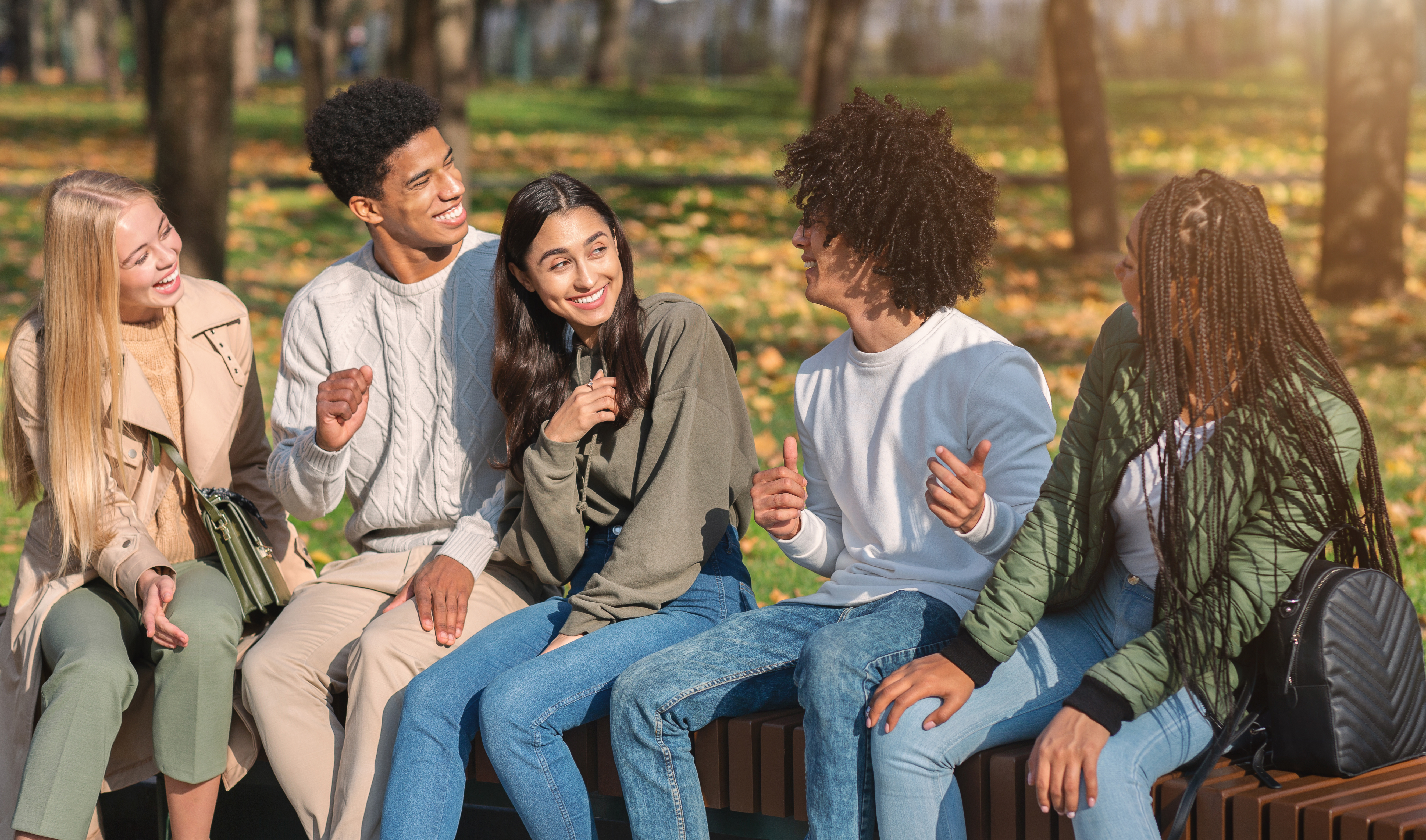 a group of young people sit in a park and laugh together