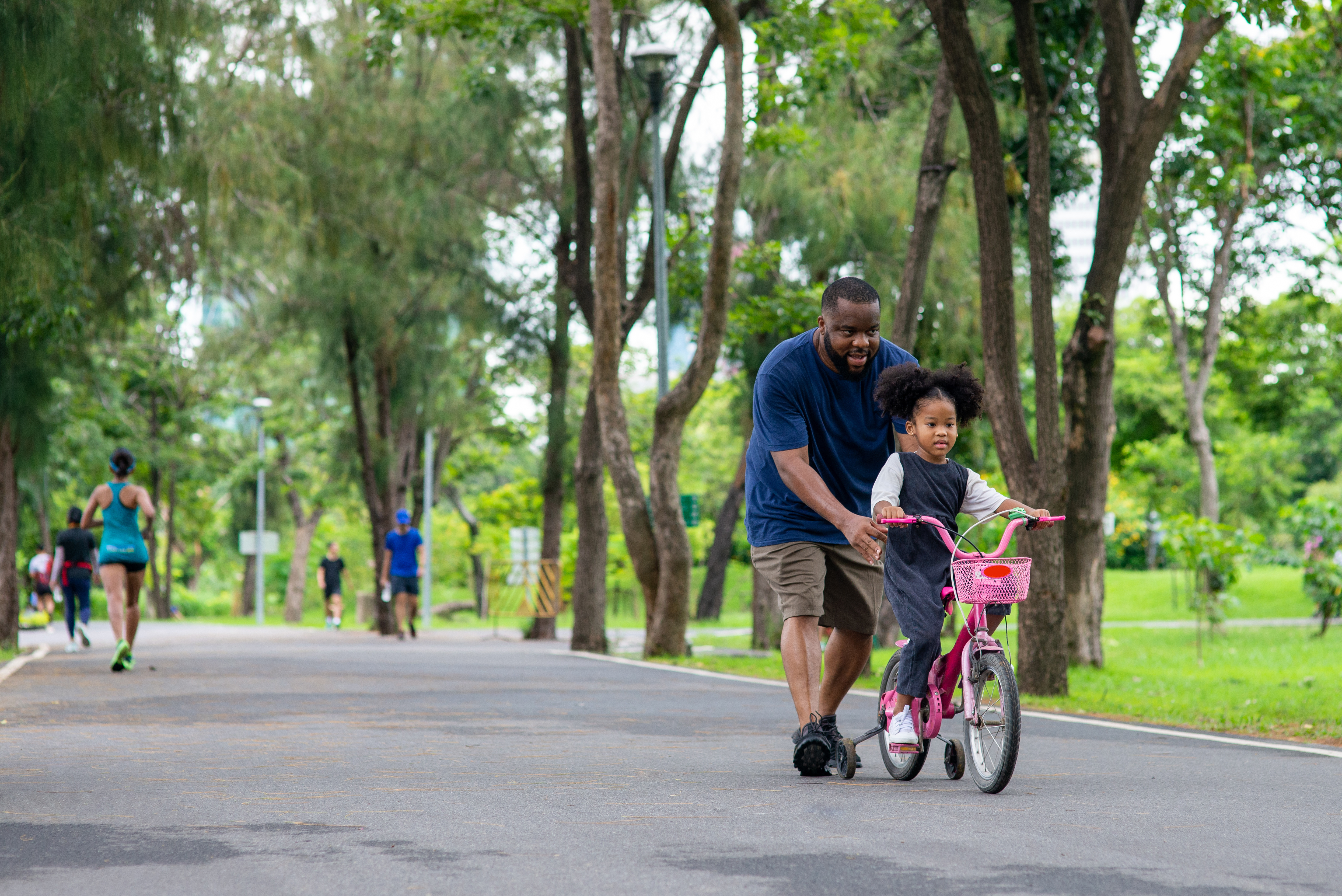 a little girl rides a bike with the help of an adult