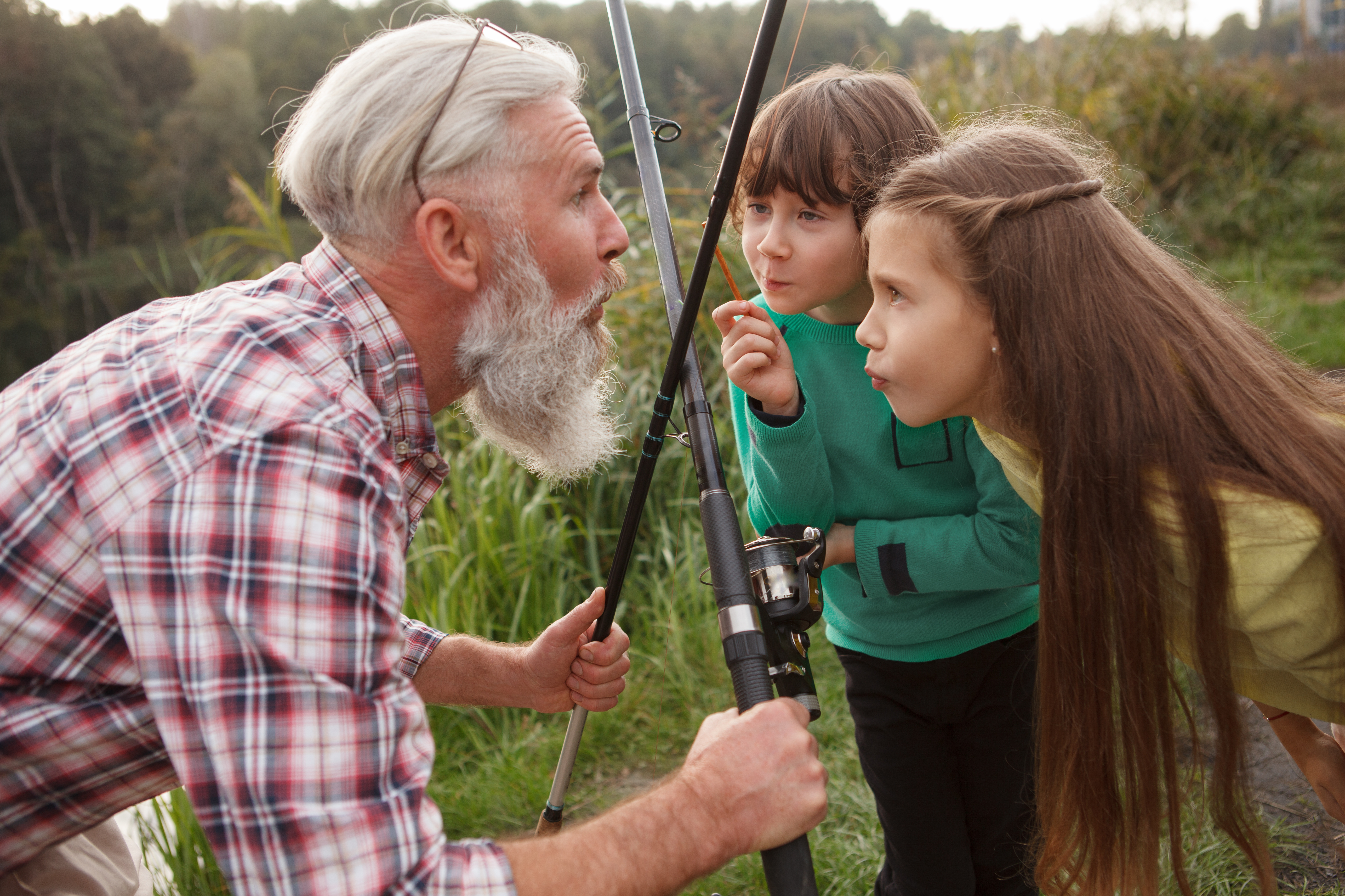 Two kids smile at an older man holding fishing poles