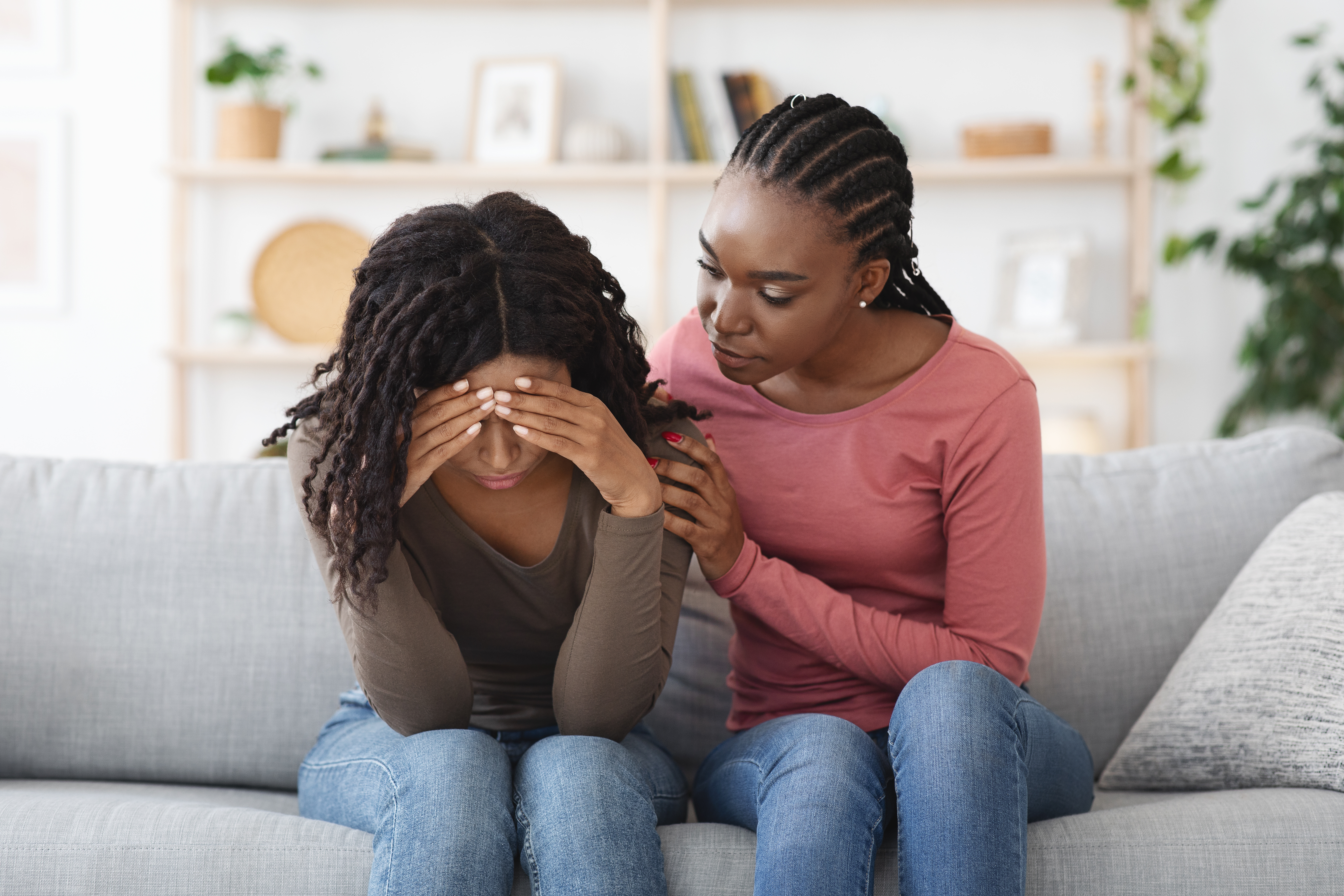 Two people sit on a couch, one comforting the other